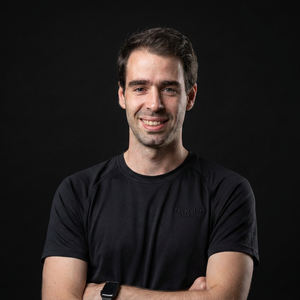Smiling man in a black T-shirt with arms crossed against a dark background