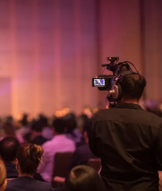 A video camera records a banquet hall set.