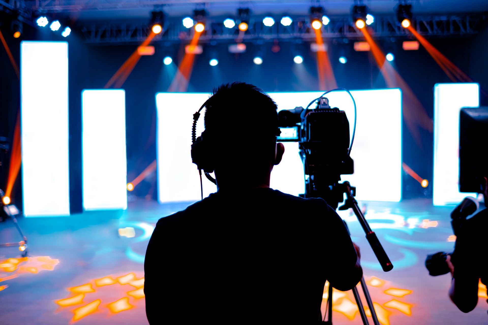 Silhouette of a camera operator filming a brightly lit stage with LED screens and spotlights