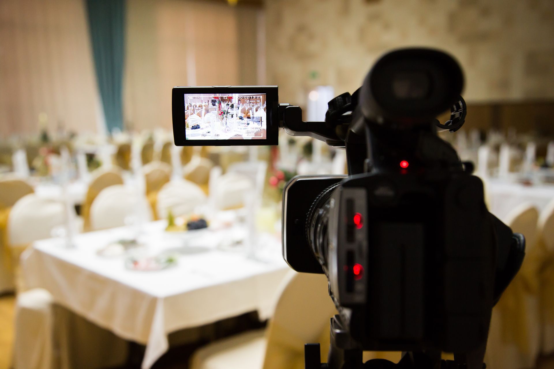 A video camera records a banquet hall set.