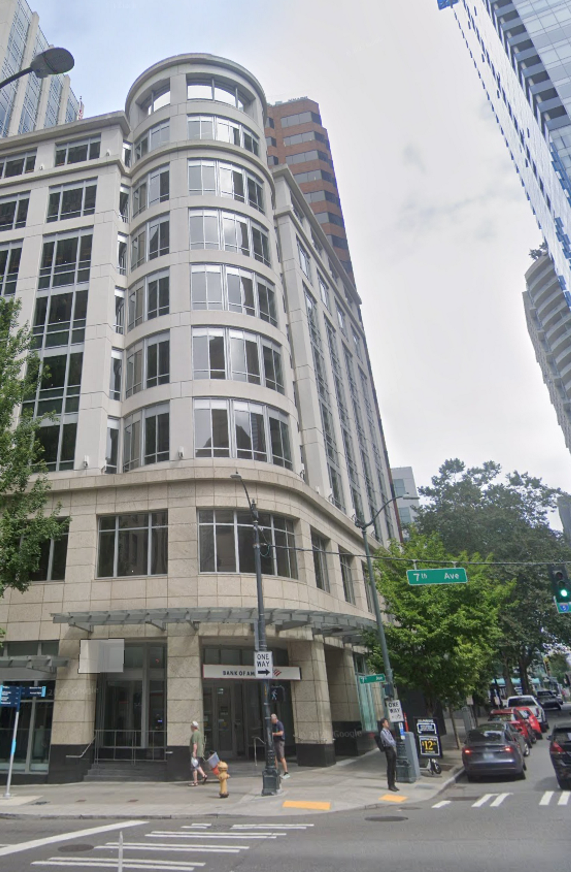 Tall rounded corner building on a city street with pedestrians and cars near a crosswalk