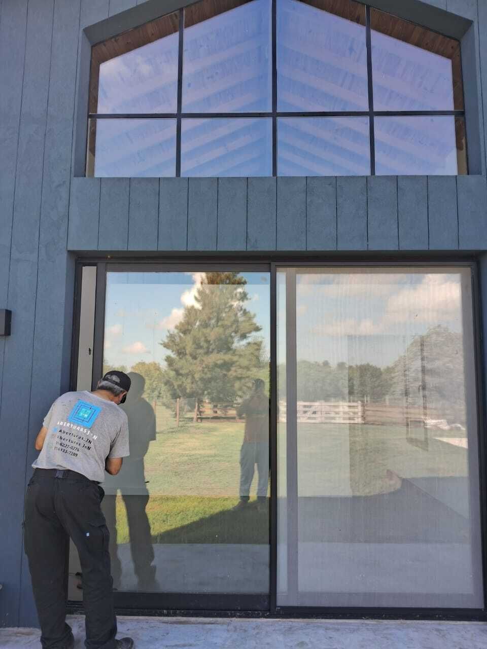 Persona trabajando en una puerta corrediza de vidrio; edificio azul con una gran ventana 