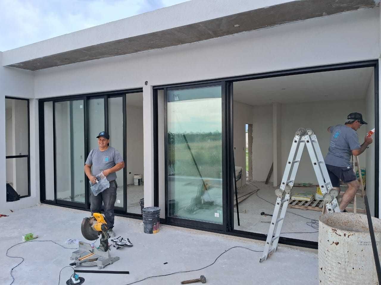Dos trabajadores durante la construcción de una casa, cerca de puertas corredizas de vidrio. 