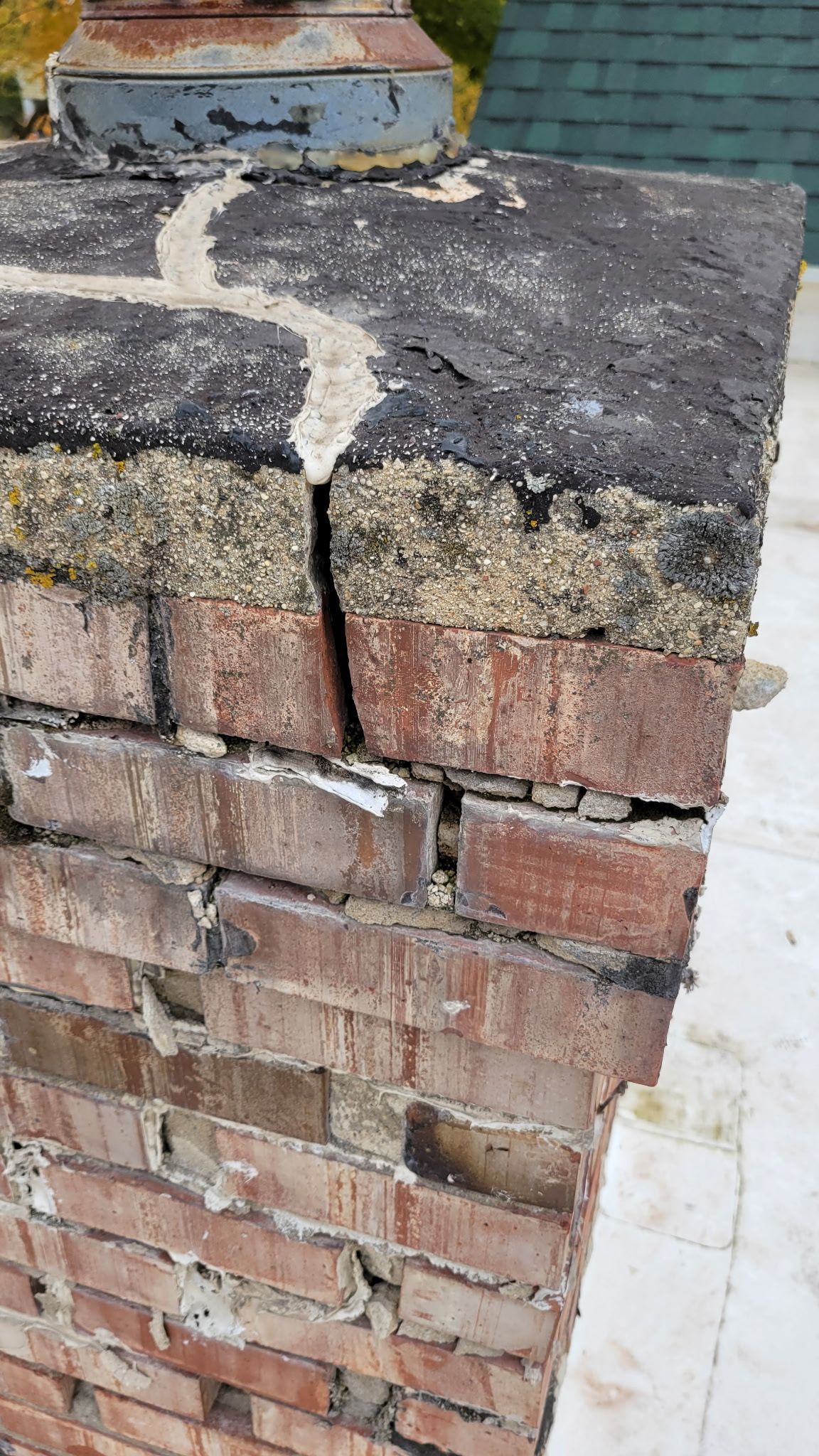 Close-up of a damaged brick chimney with a cracked top and deteriorating mortar, revealing layered materials.
