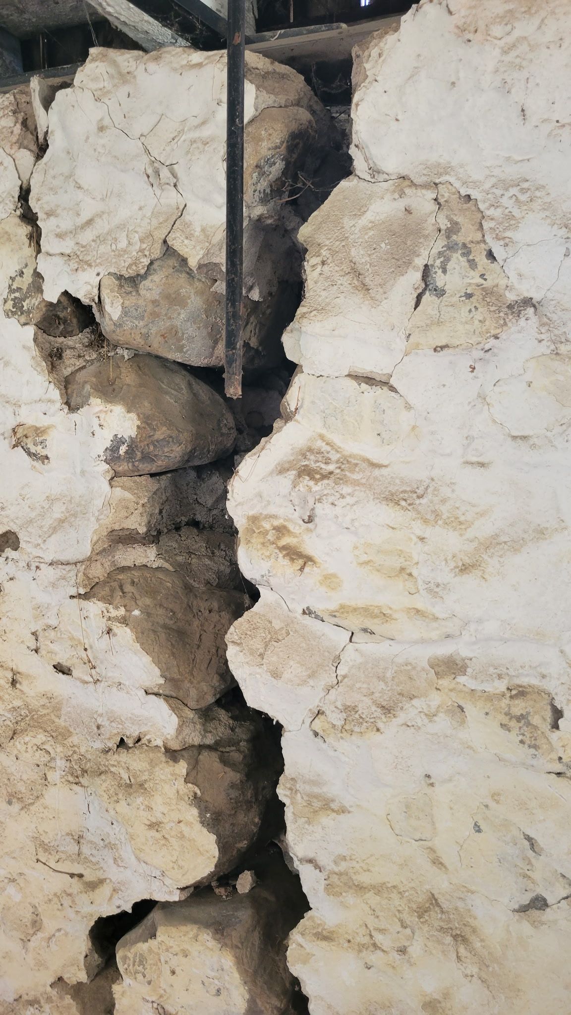 Large crack in a stone and plaster wall.  Dark interior, possibly a building foundation.