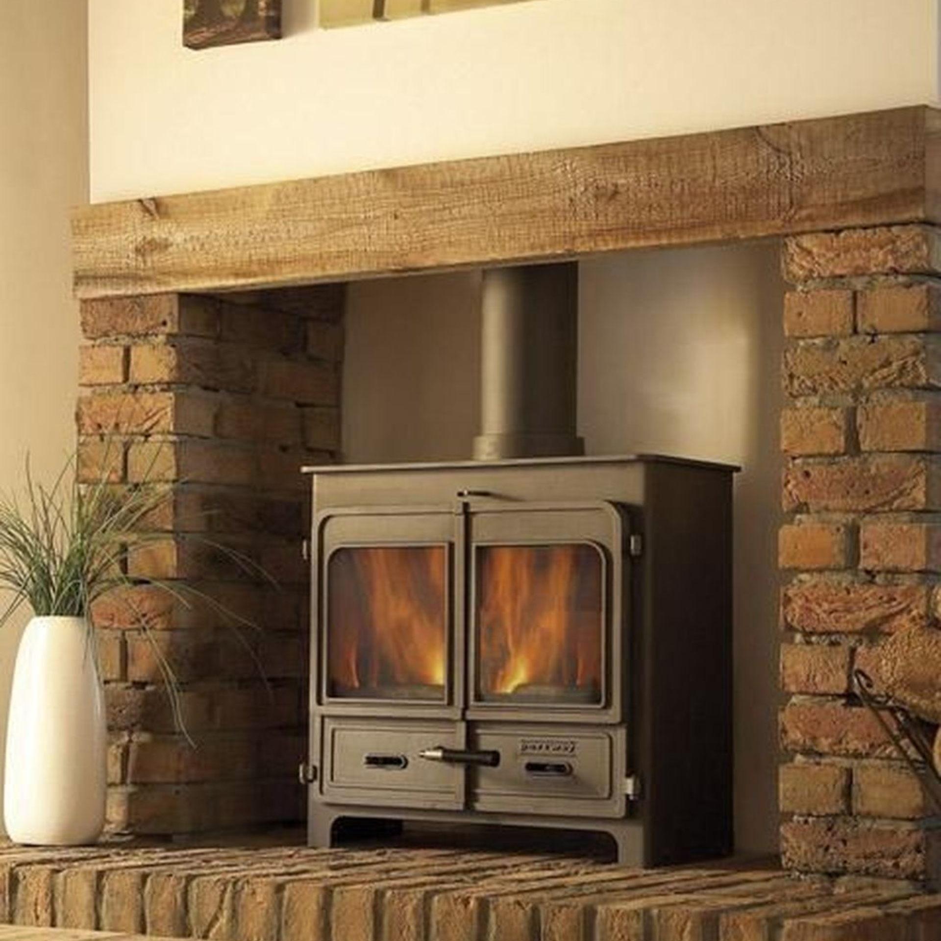 Wood-burning stove inside a brick fireplace, under a wooden mantel. Flames visible through glass doors.
