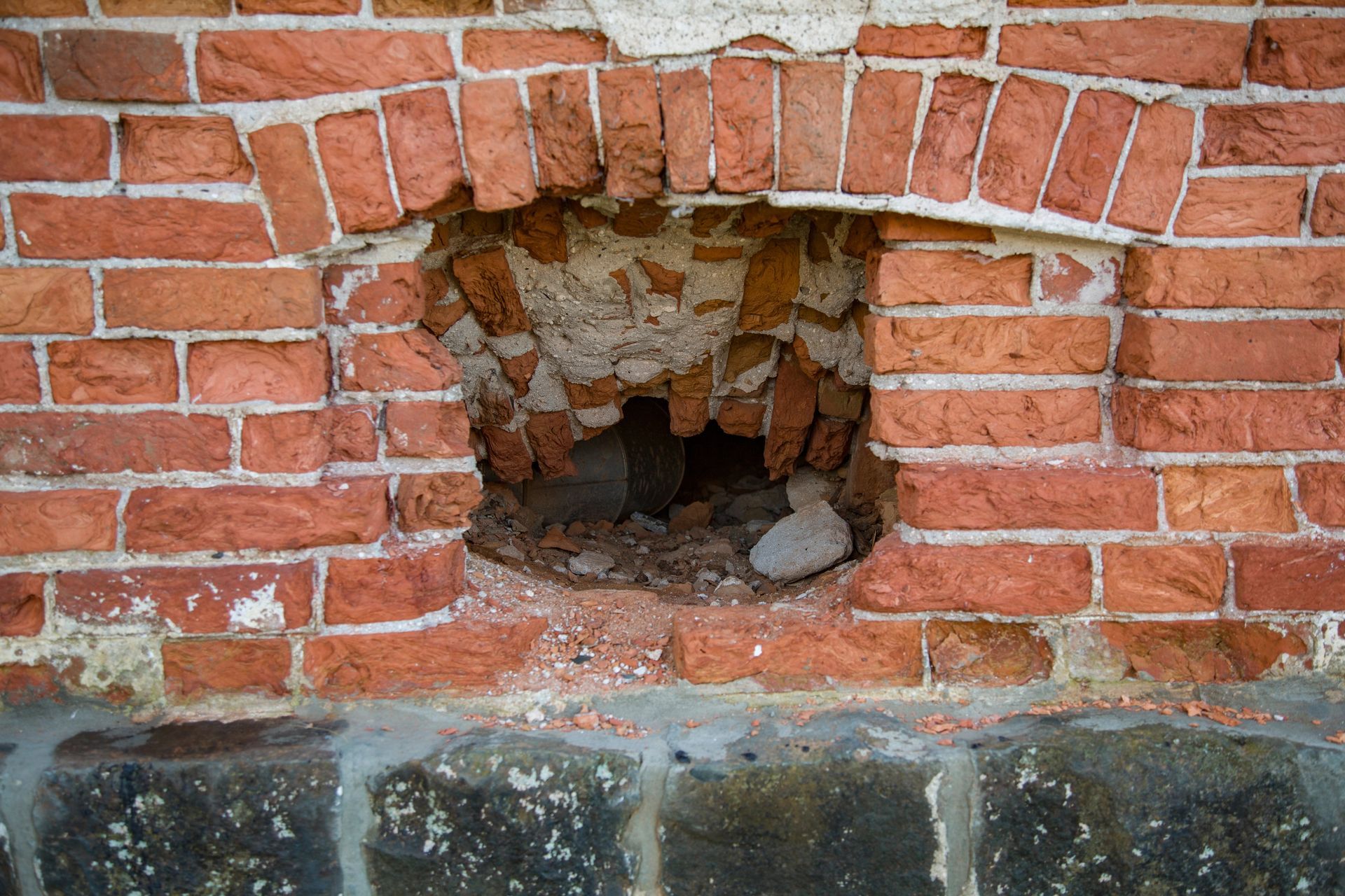 Brick wall with a damaged opening. Red bricks, crumbling mortar, opening reveals interior.