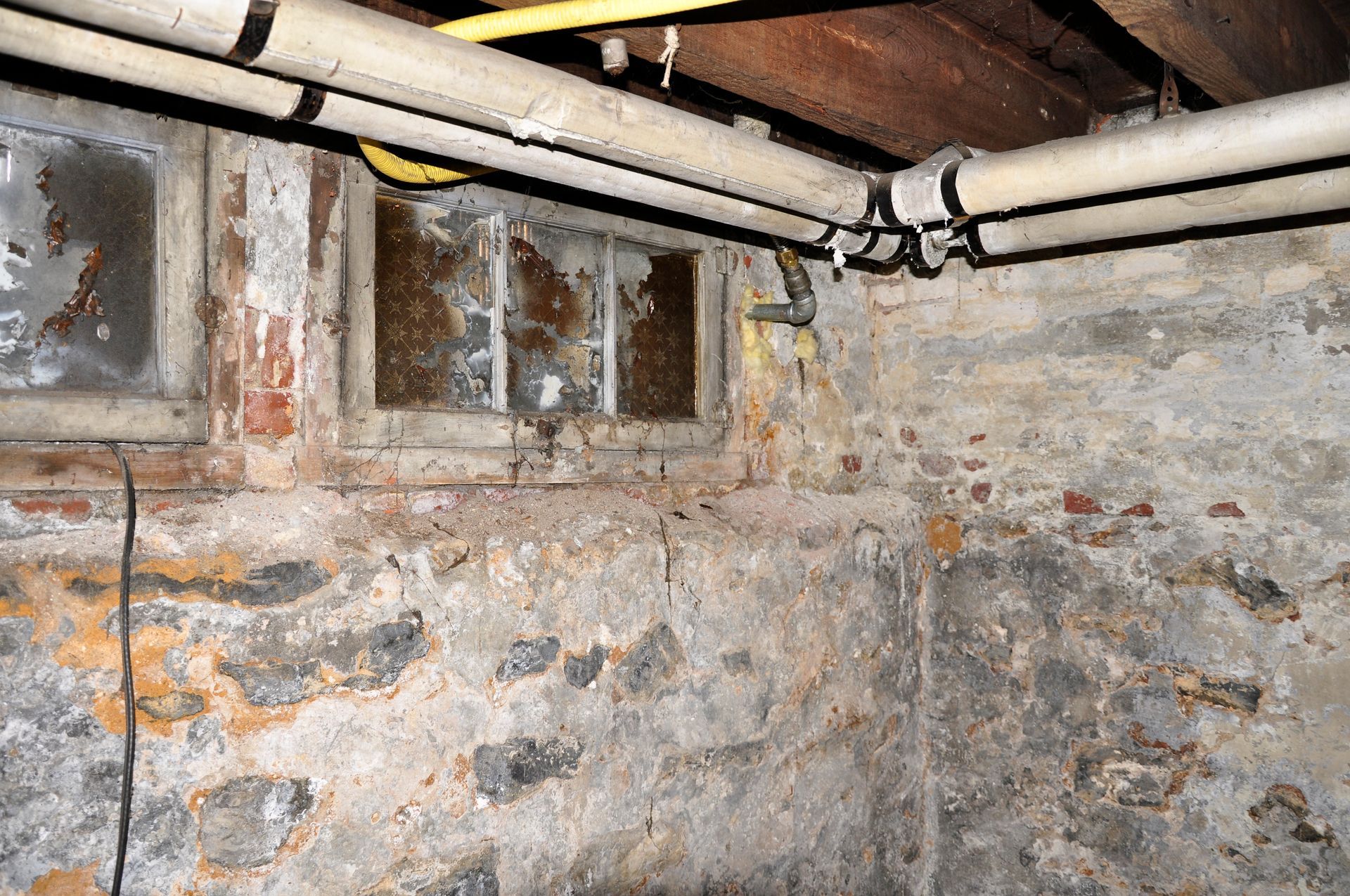 A basement with a brick wall and pipes hanging from the ceiling