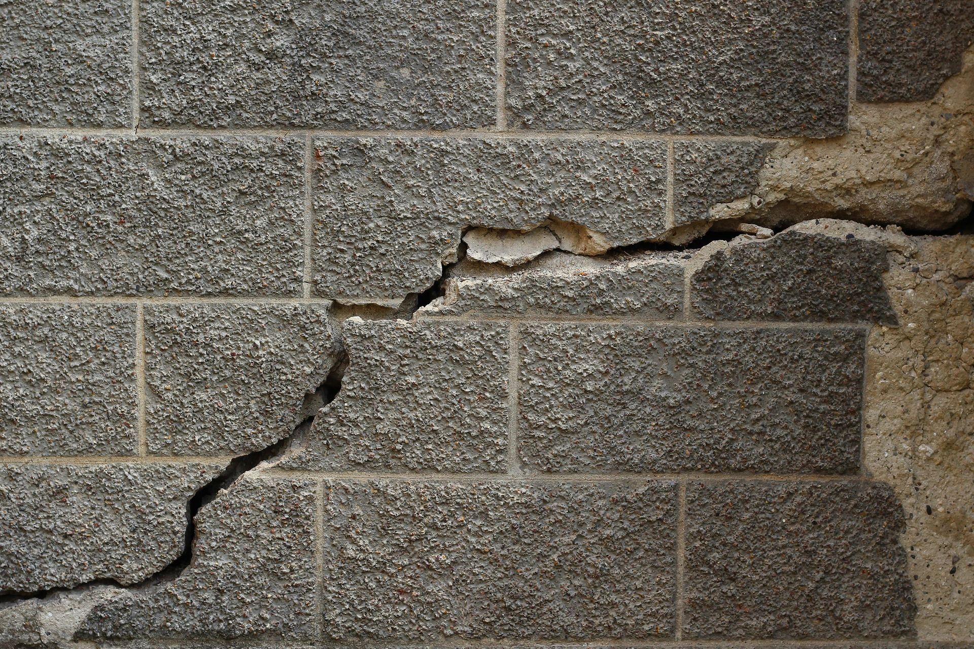 Cracked concrete block wall, gray, with a large horizontal crack and crumbling edges.