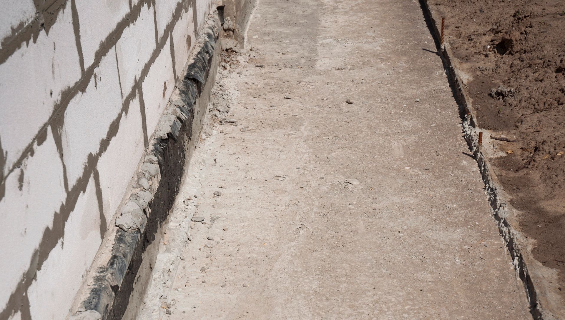 A white brick wall with a concrete sidewalk in front of it.