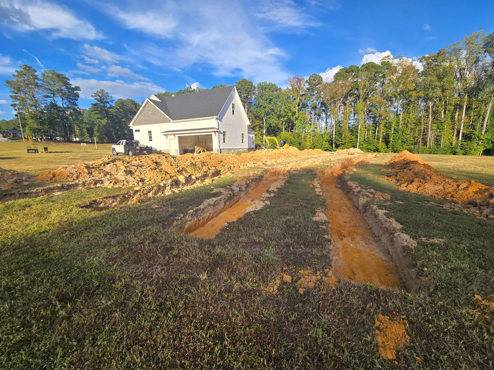 Fresh soil paths in a rural yard leading to a white house under a blue sky, with trees in the background