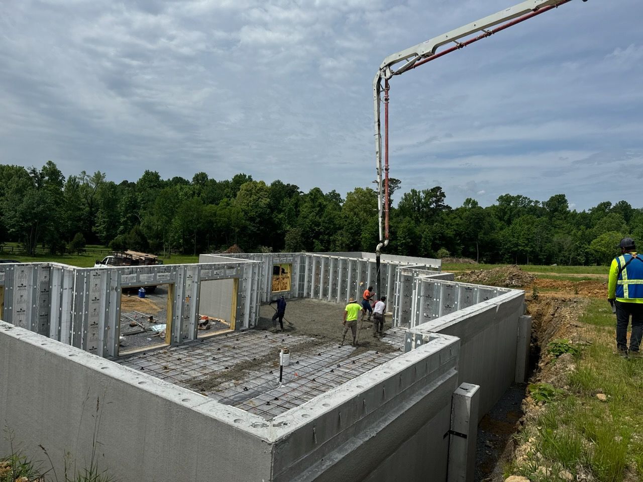 Construction workers pouring concrete into a building foundation with concrete walls and a pump boom overhead