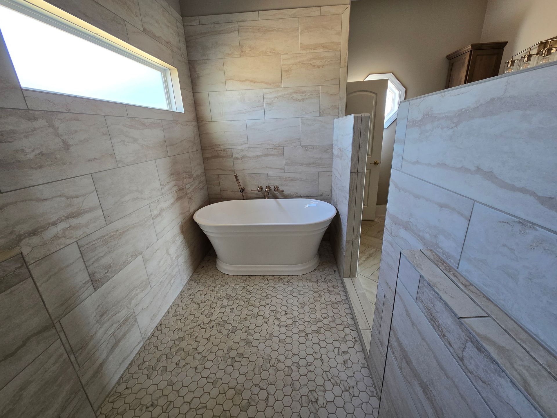 Modern bathroom with a freestanding tub, stone-look walls, narrow window, and patterned tile floor