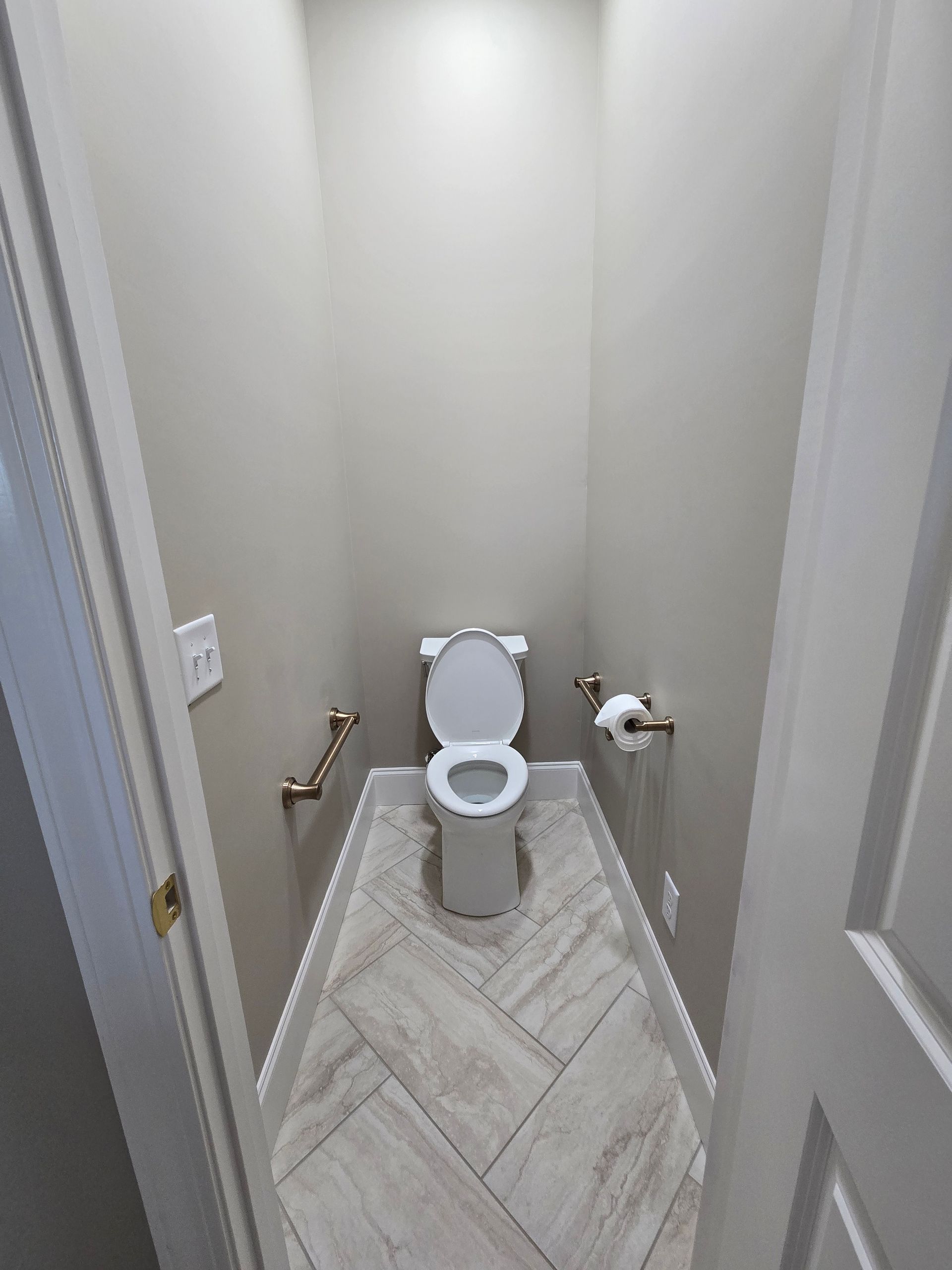 Small narrow bathroom with an open toilet and herringbone tile floor.
