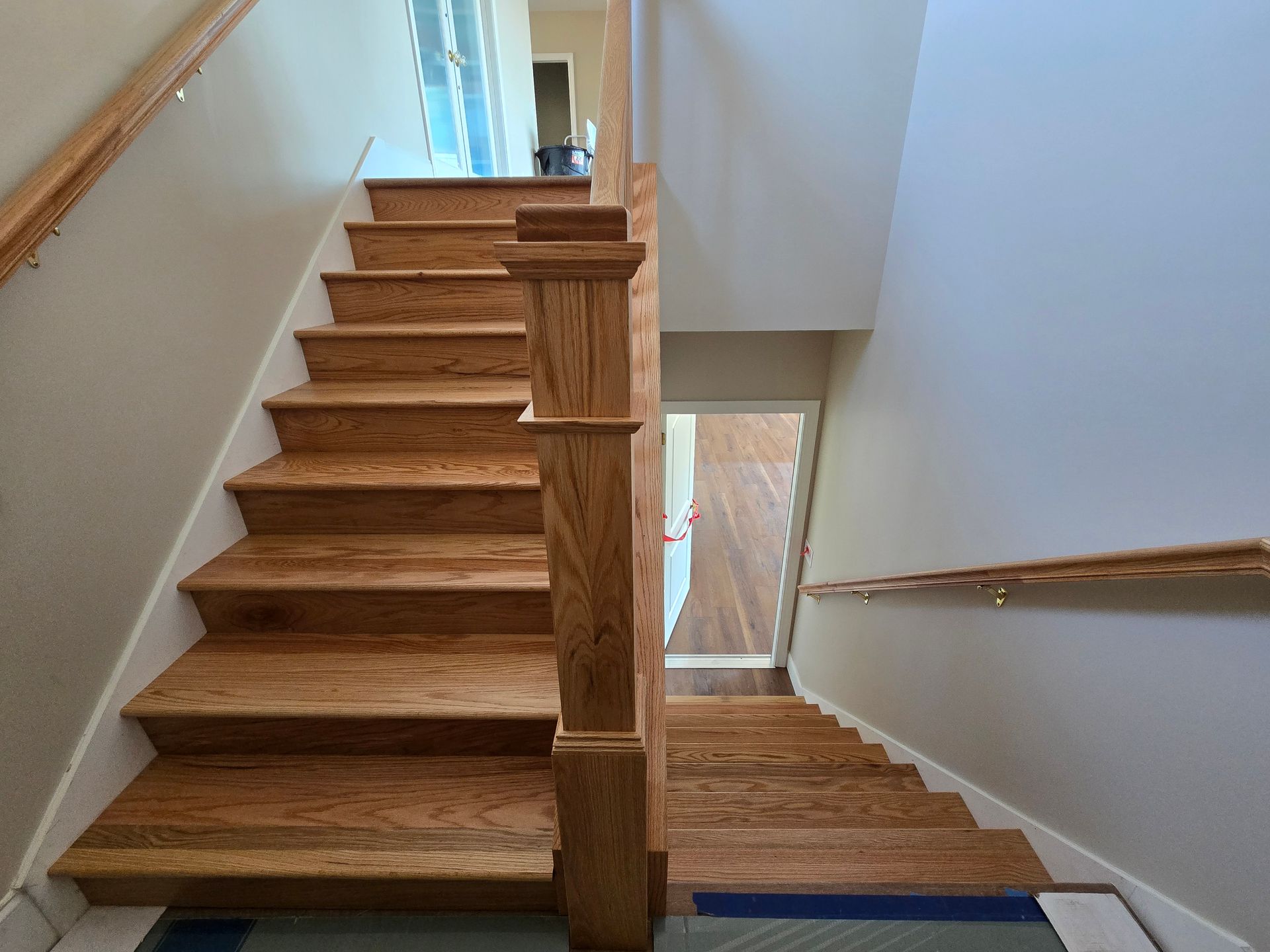 Wooden staircase with white walls and a central landing, viewed from top and bottom at once