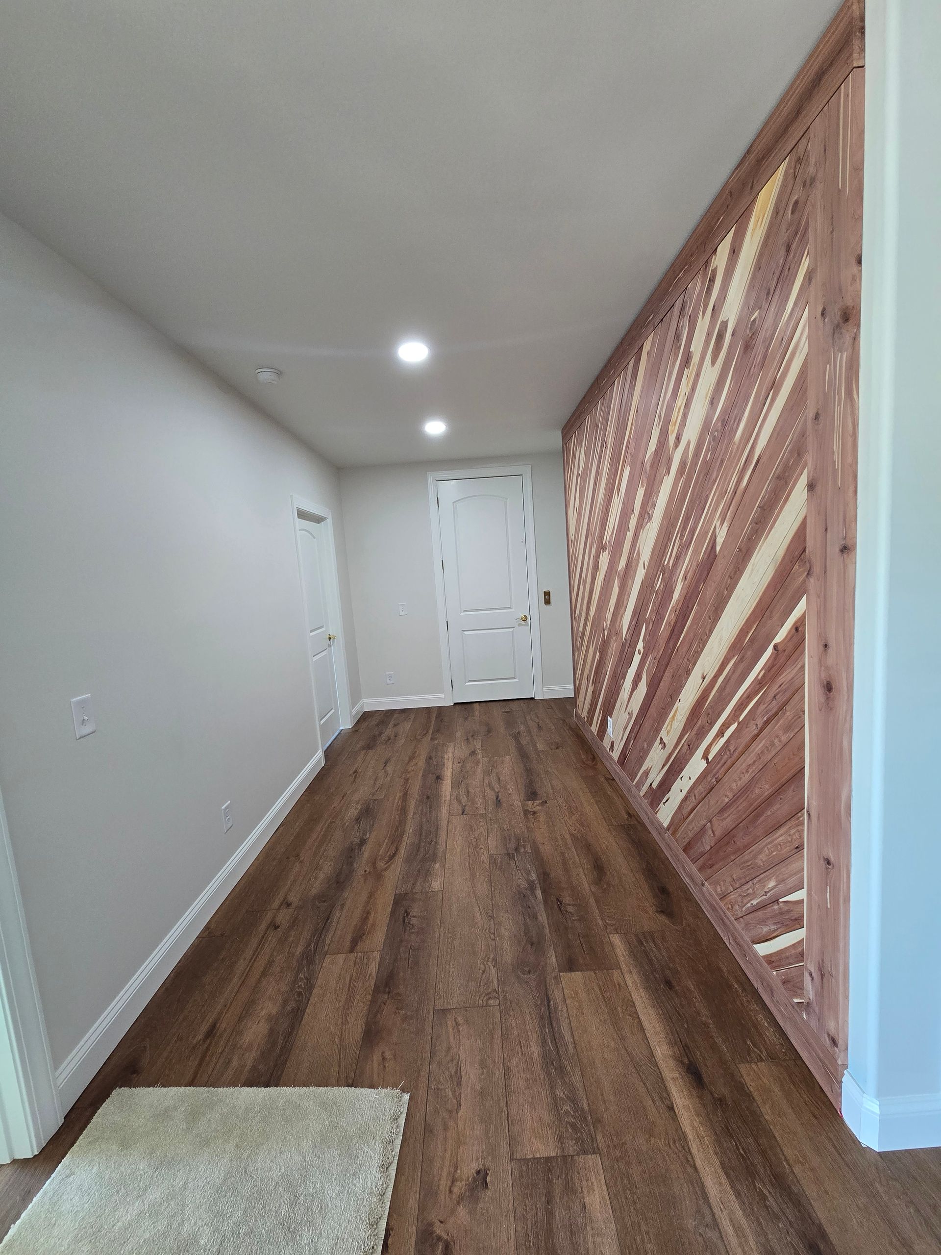 Narrow hallway with wood floors, white walls, recessed lights, and a patterned accent wall at the end.