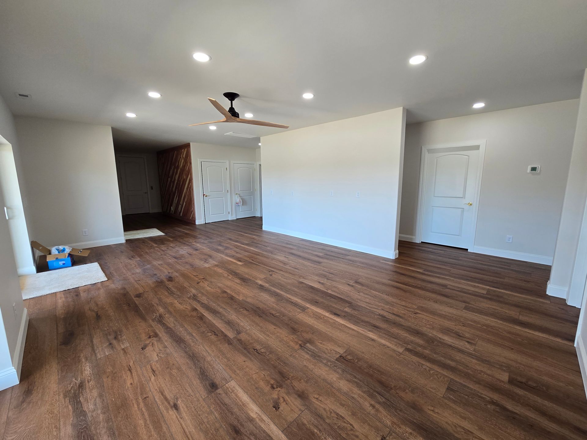 Empty living room with wood floors, white walls, recessed lights, and a ceiling fan