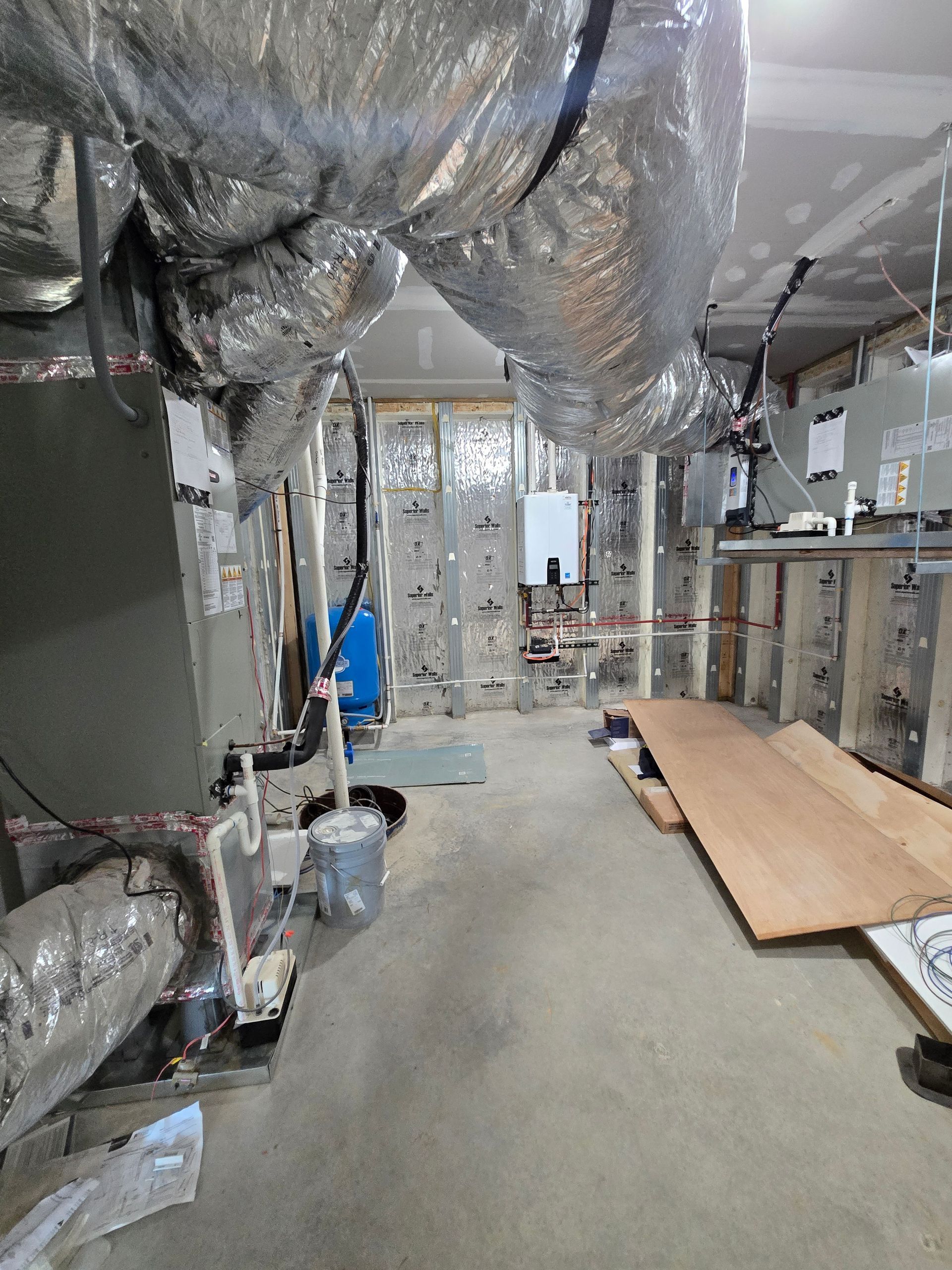 Basement utility corridor with exposed ducts, pipes, and construction materials on the floor
