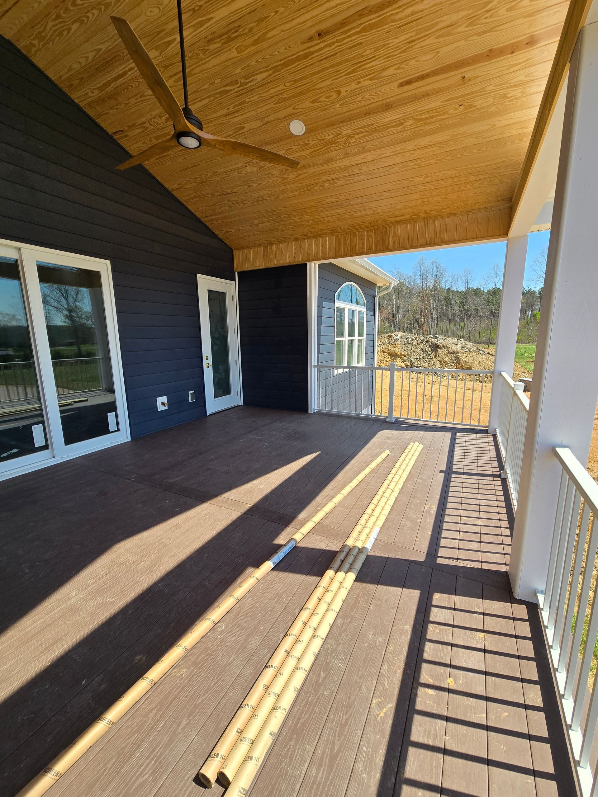Covered porch with dark siding, wood ceiling, and yellow tactile paving along the floor.