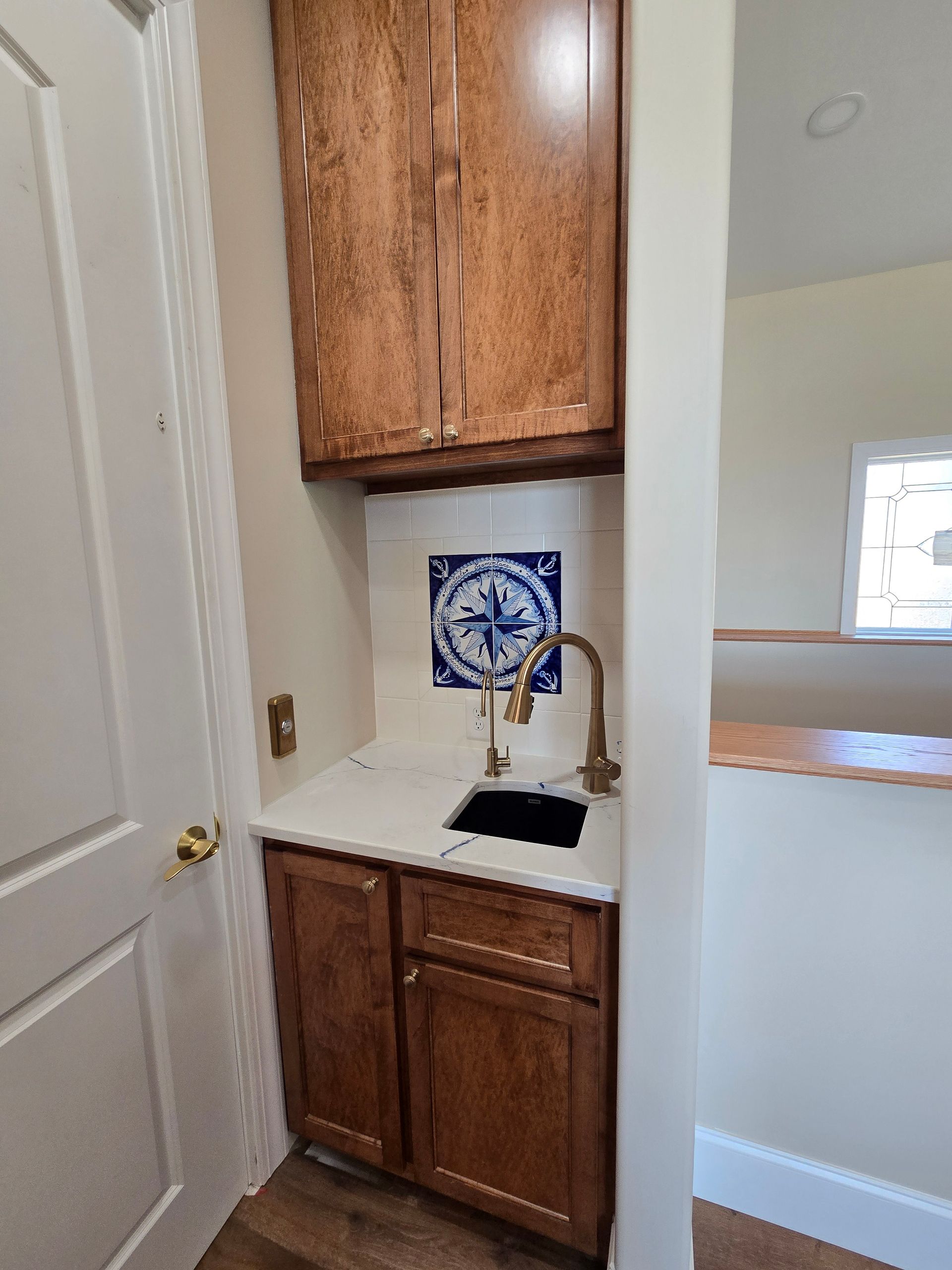 Small built-in hallway cabinet nook with white countertop, wood cabinets, sink, and blue decorative tile.