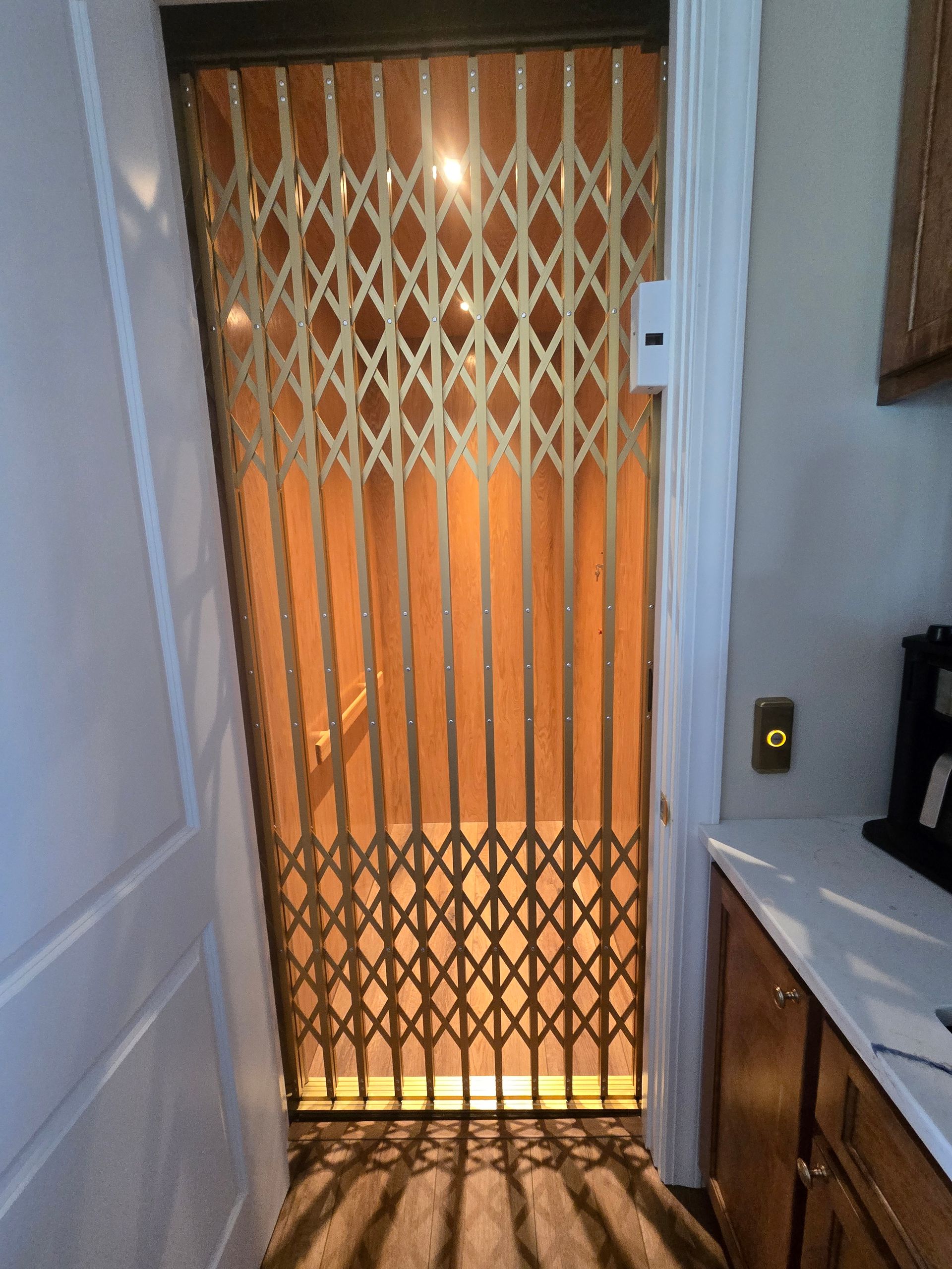 Indoor elevator with a gold accordion gate, viewed through an open doorway.