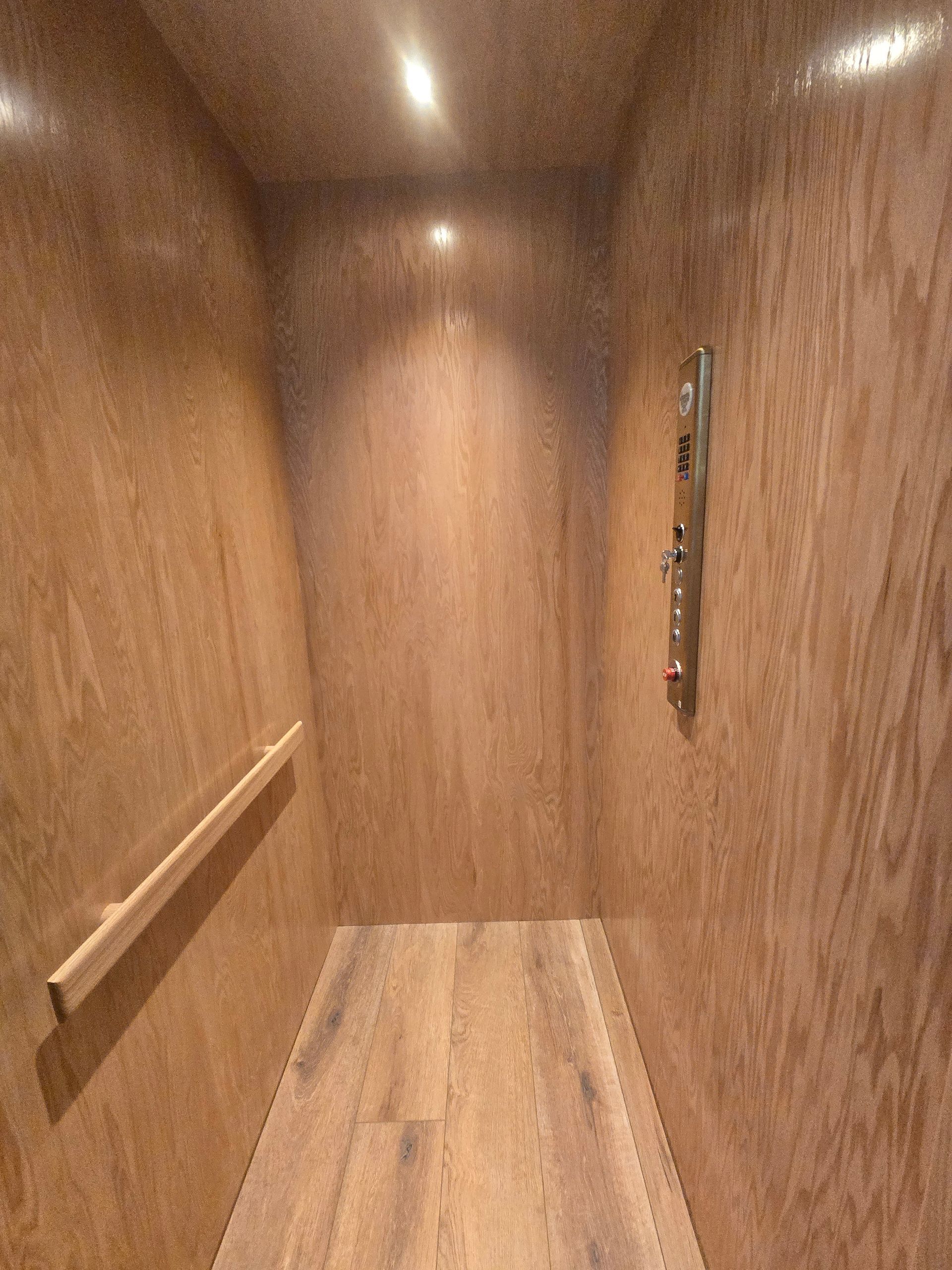 Wood-paneled elevator interior with a handrail on the left and control panel on the right.