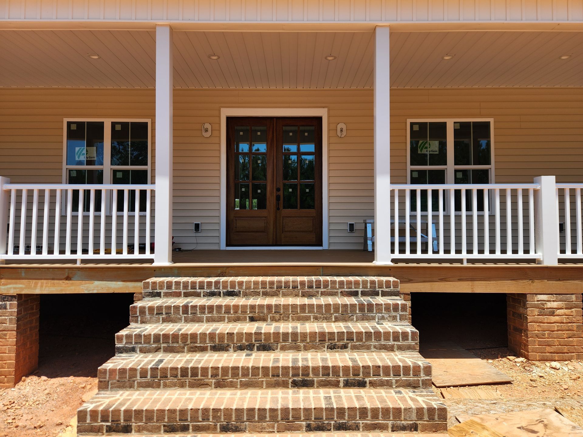 Front entrance of a tan house with white railings and brick steps leading to double wooden doors