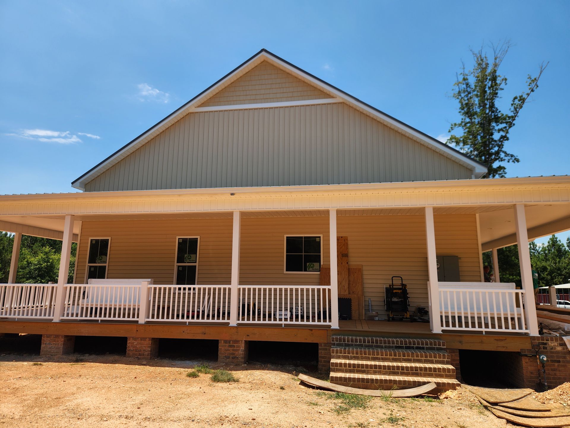 White farmhouse with a wide front porch, brick steps, and a gabled roof under a blue sky