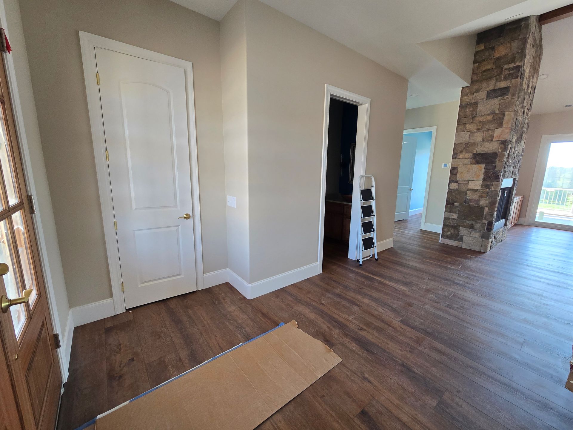 Empty modern room with hardwood floors, beige walls, a white closet door, and a stone fireplace column.