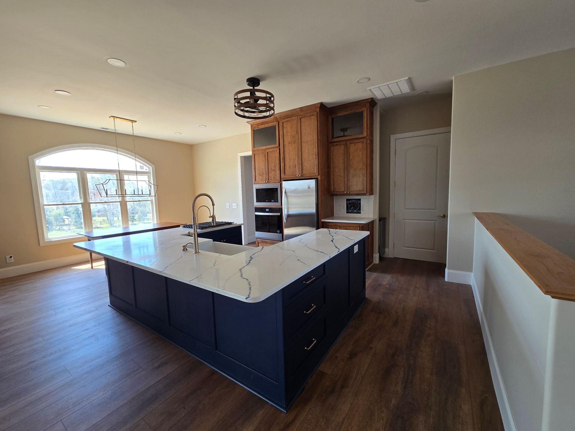 Spacious modern kitchen with dark island, white countertops, wood cabinets, and large window