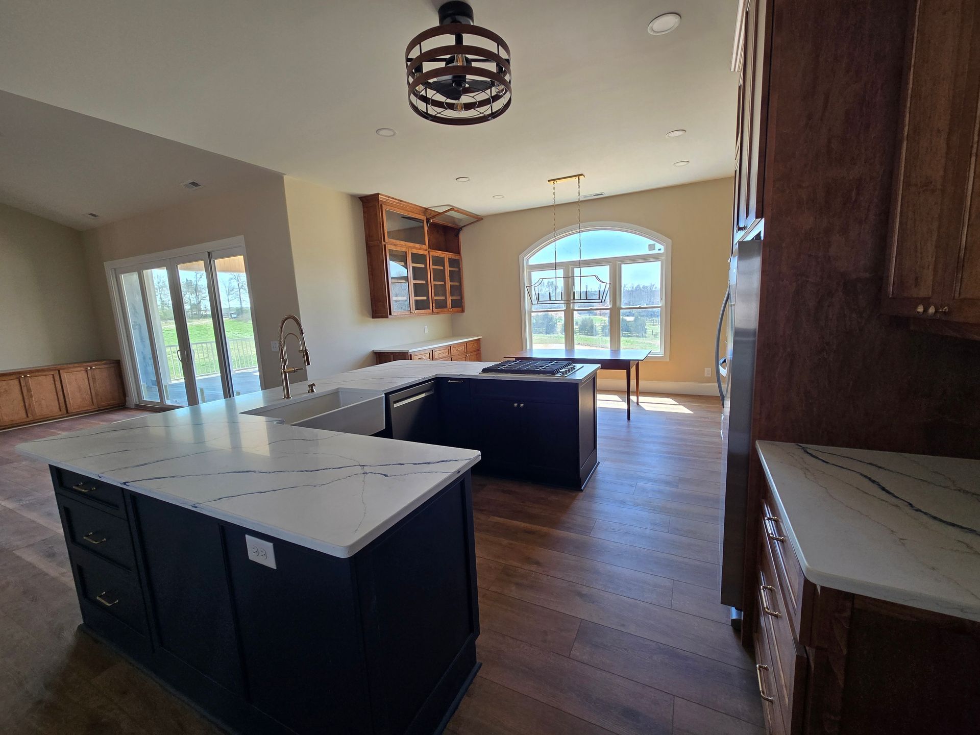 Bright kitchen with dark island, white countertops, wood floors, and large windows opening to a patio