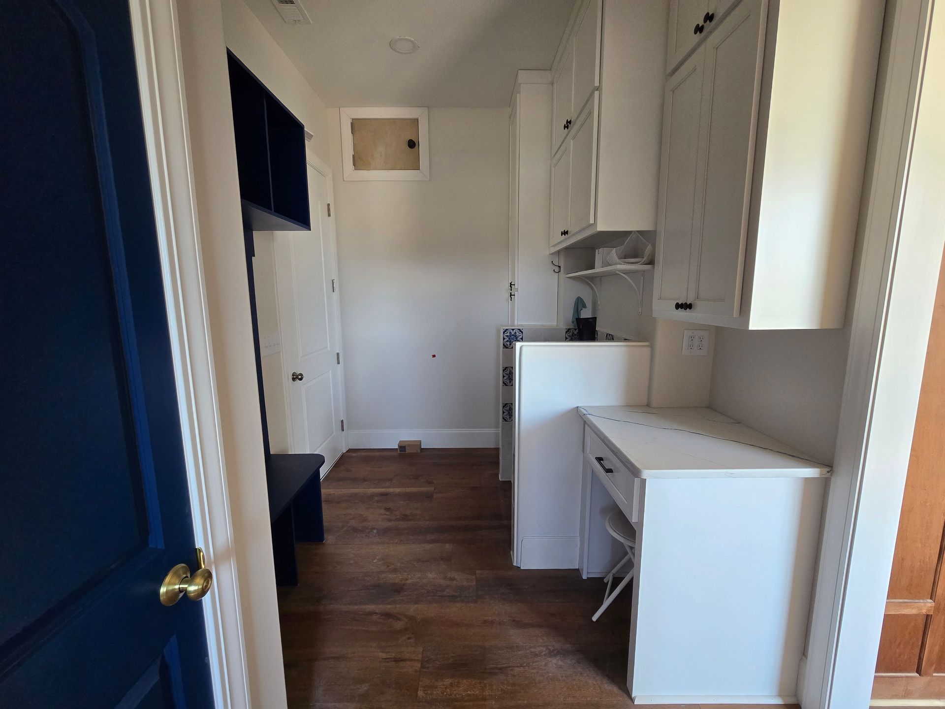 Narrow hallway with blue walls and white cabinets, leading to a small kitchen area with wooden floors.