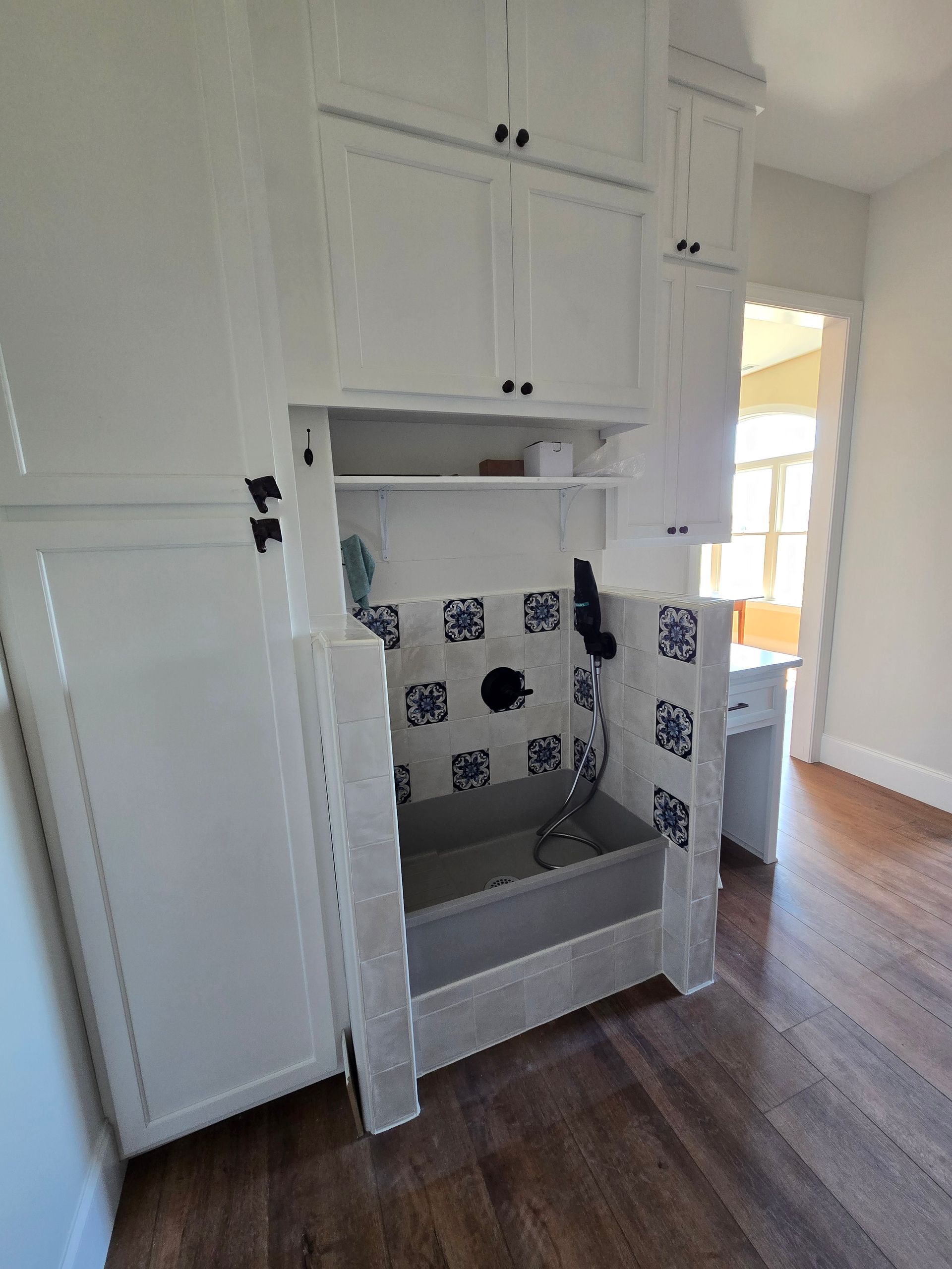 White kitchen cabinet with open under-sink space, gray sink basin, and wood floor.