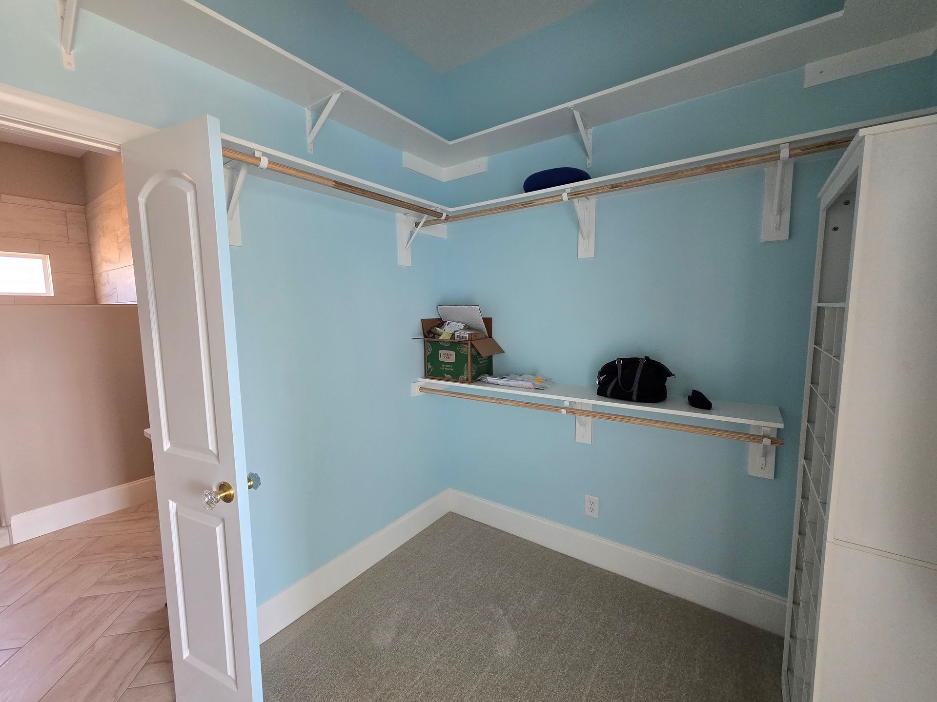 Empty light-blue bedroom or closet with white shelving and open door, viewed from the doorway