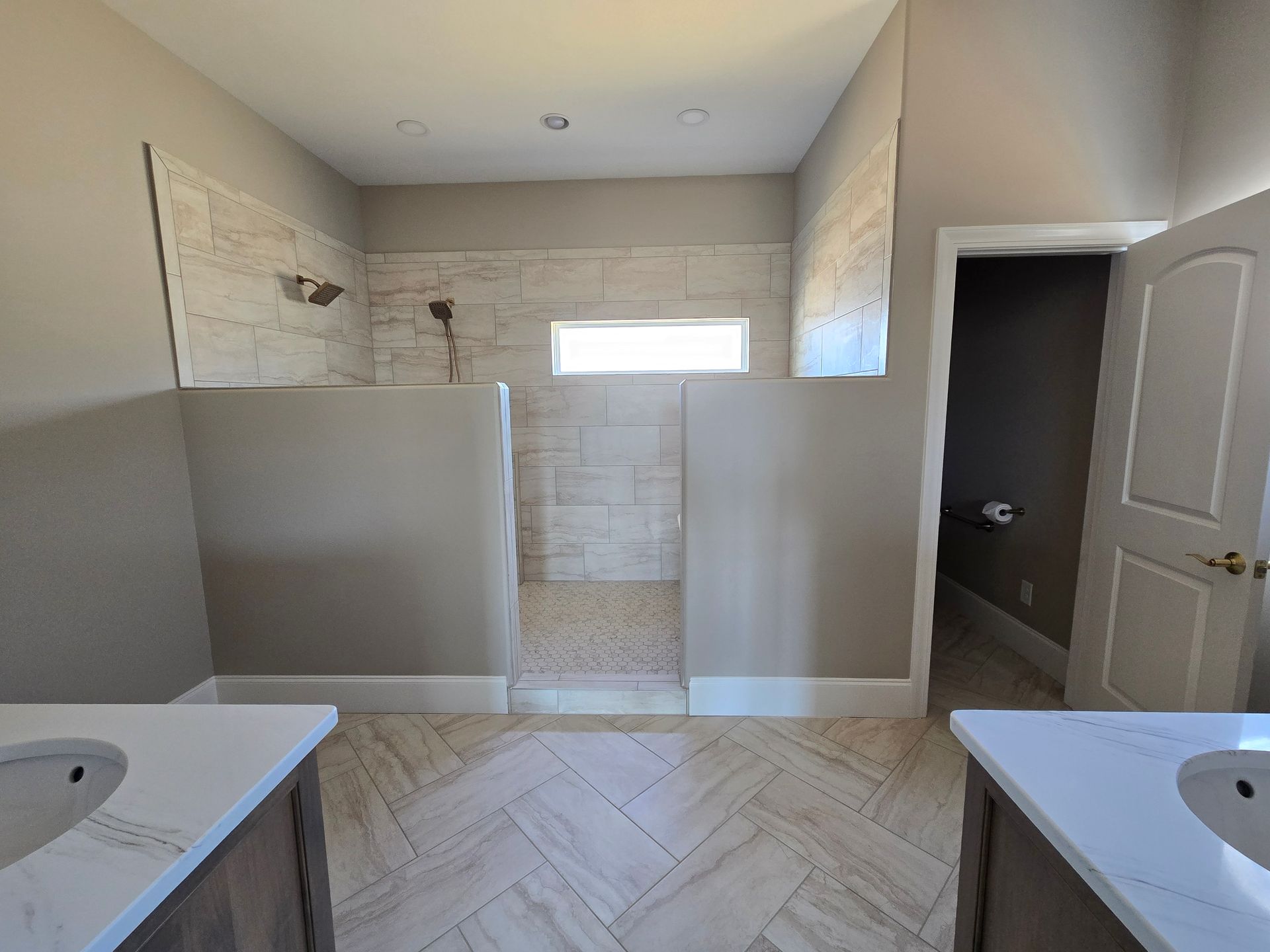 Bathroom with twin sinks, half-height partitions, tiled shower area, and an open door to the right