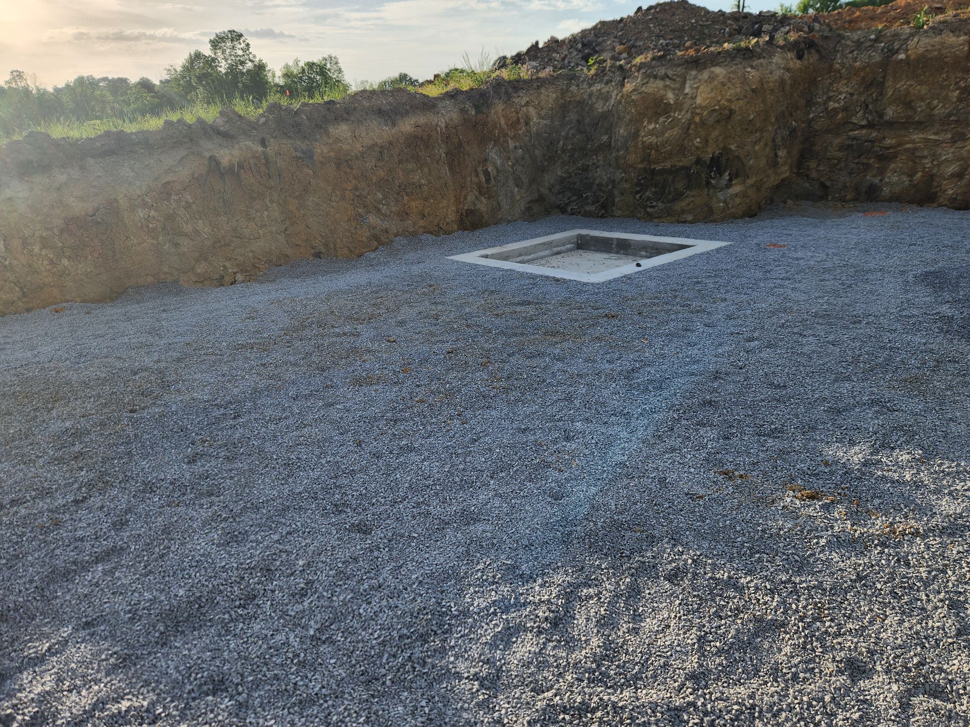 Gravel lot beside an excavated dirt embankment with a concrete pad in the center
