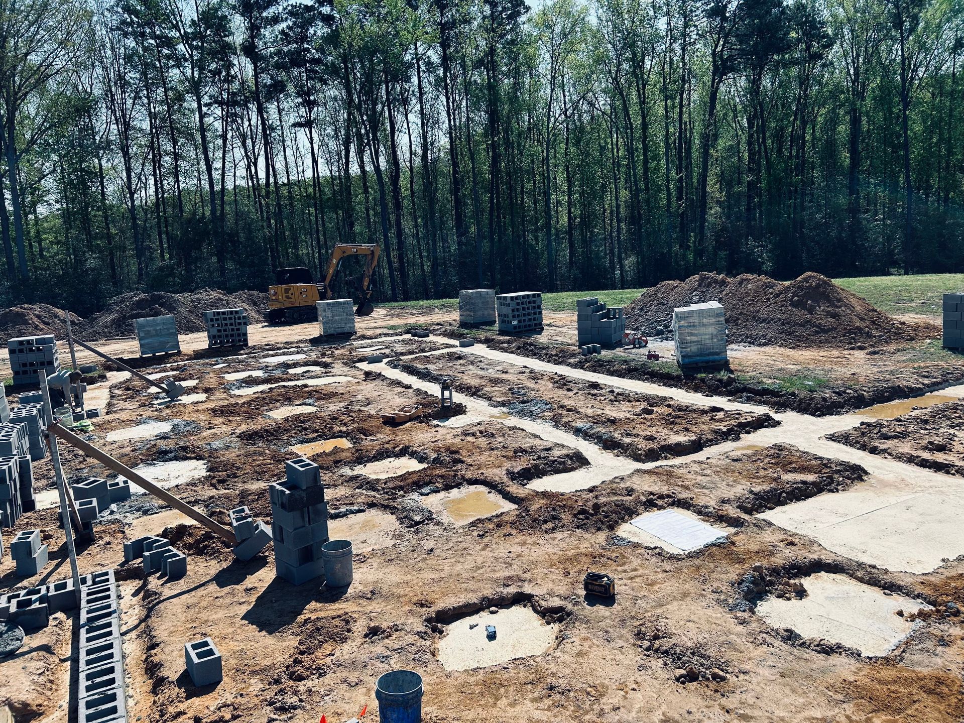 Cleared construction site with foundation blocks and materials beside a wooded tree line