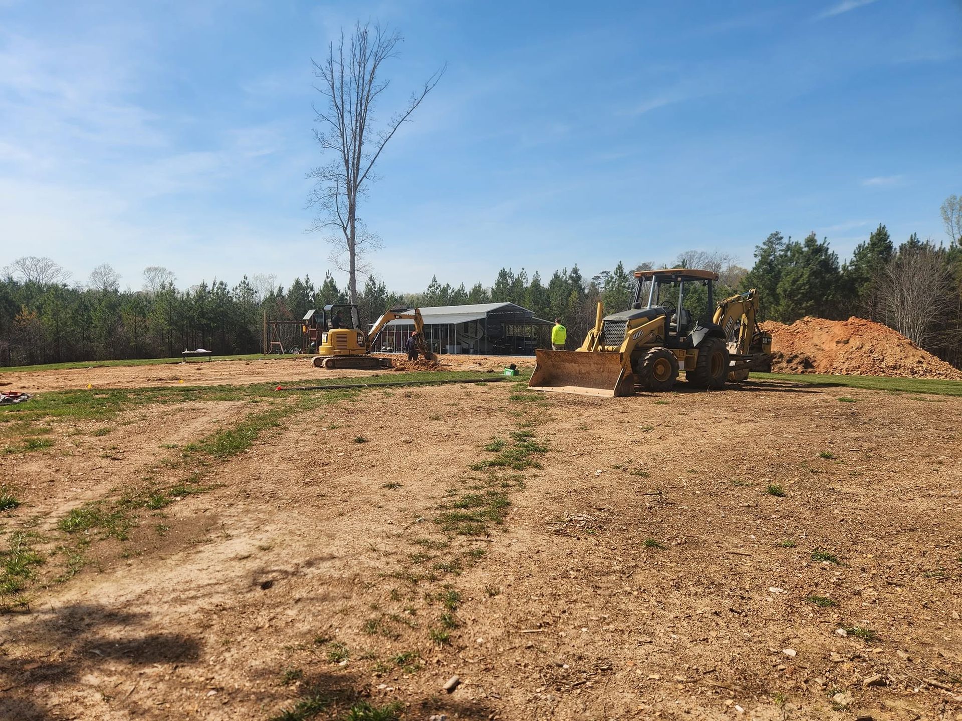 Construction site with bulldozers clearing dirt near a large soil pile under a blue sky