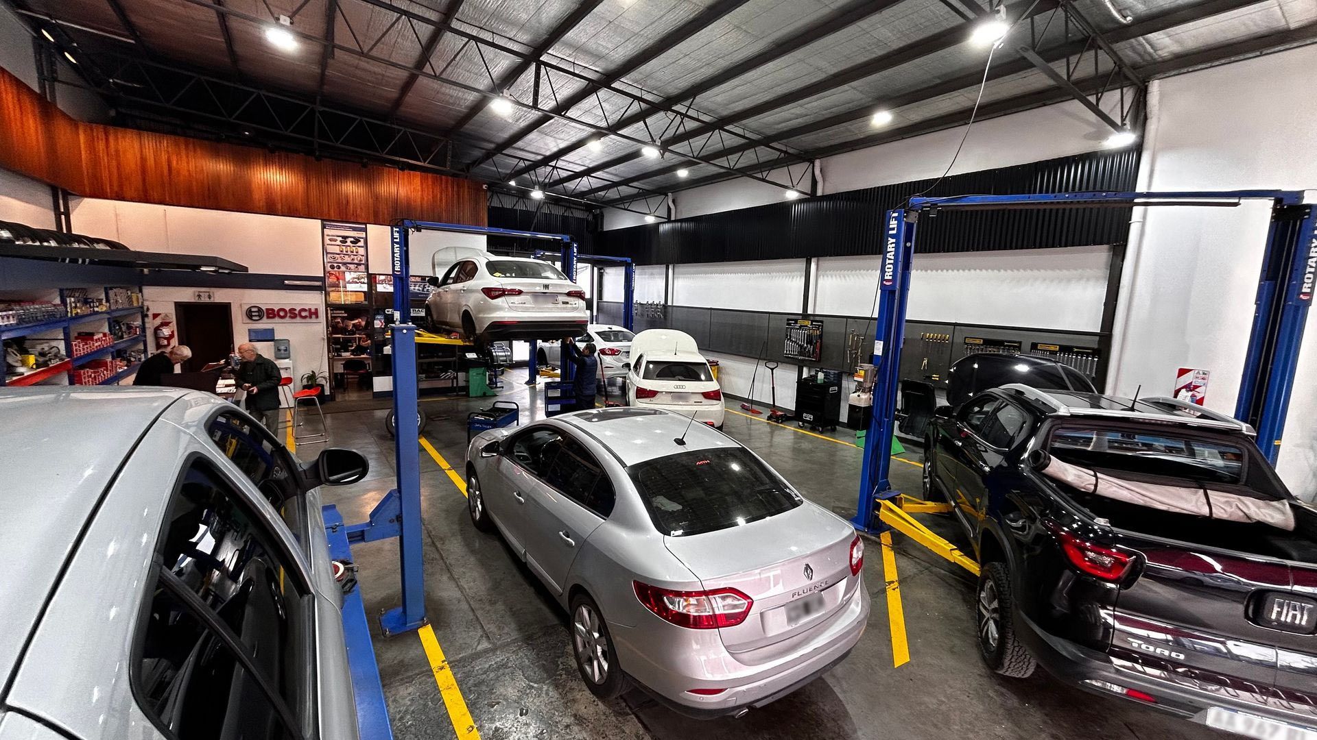 Taller mecánico con varios coches en boxes de servicio bajo luces brillantes.