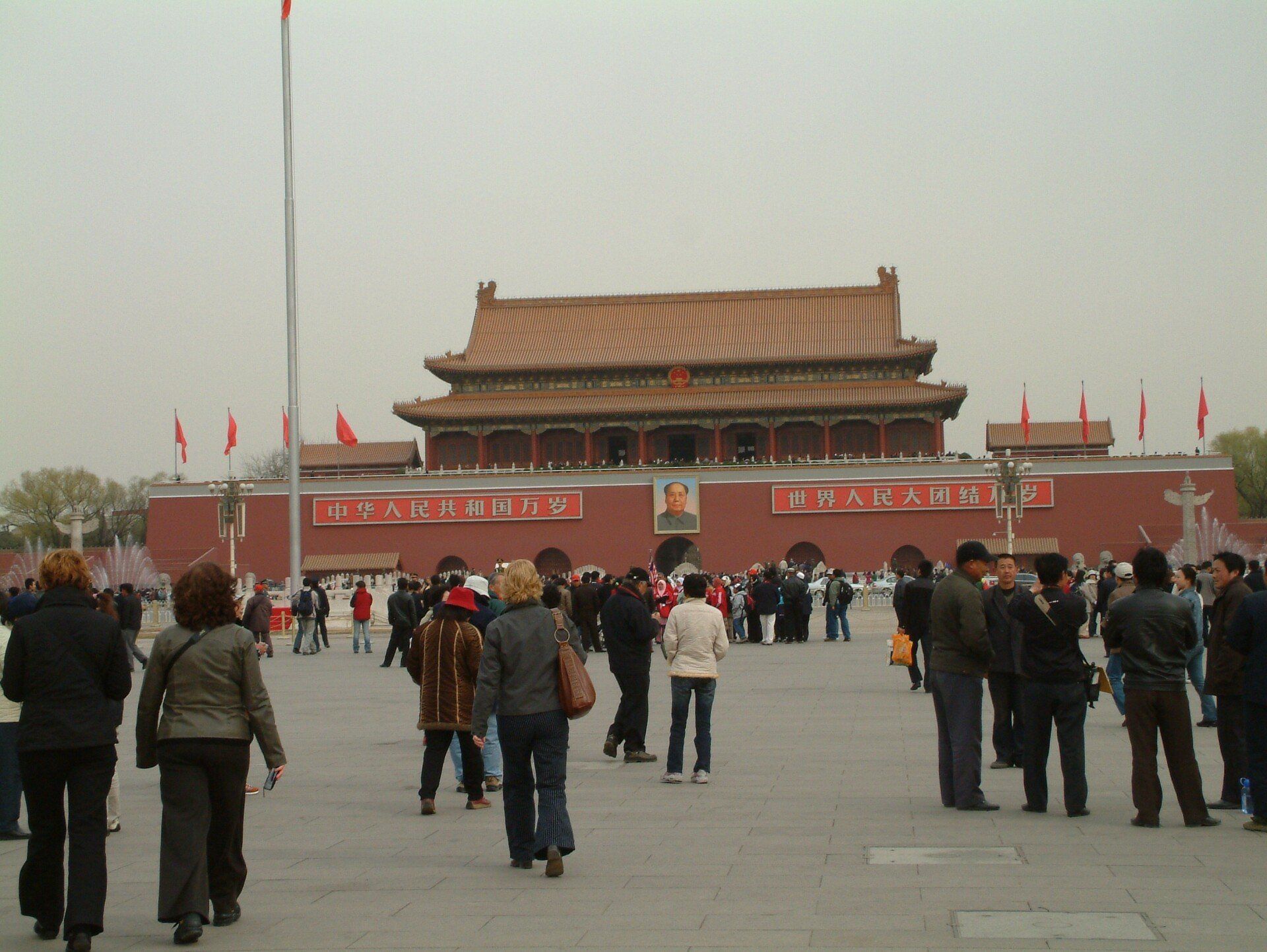 De Tiananmenpoort in Peking, vol met toeristen; rode muren, pannendak, portret van Mao, bewolkte lucht.