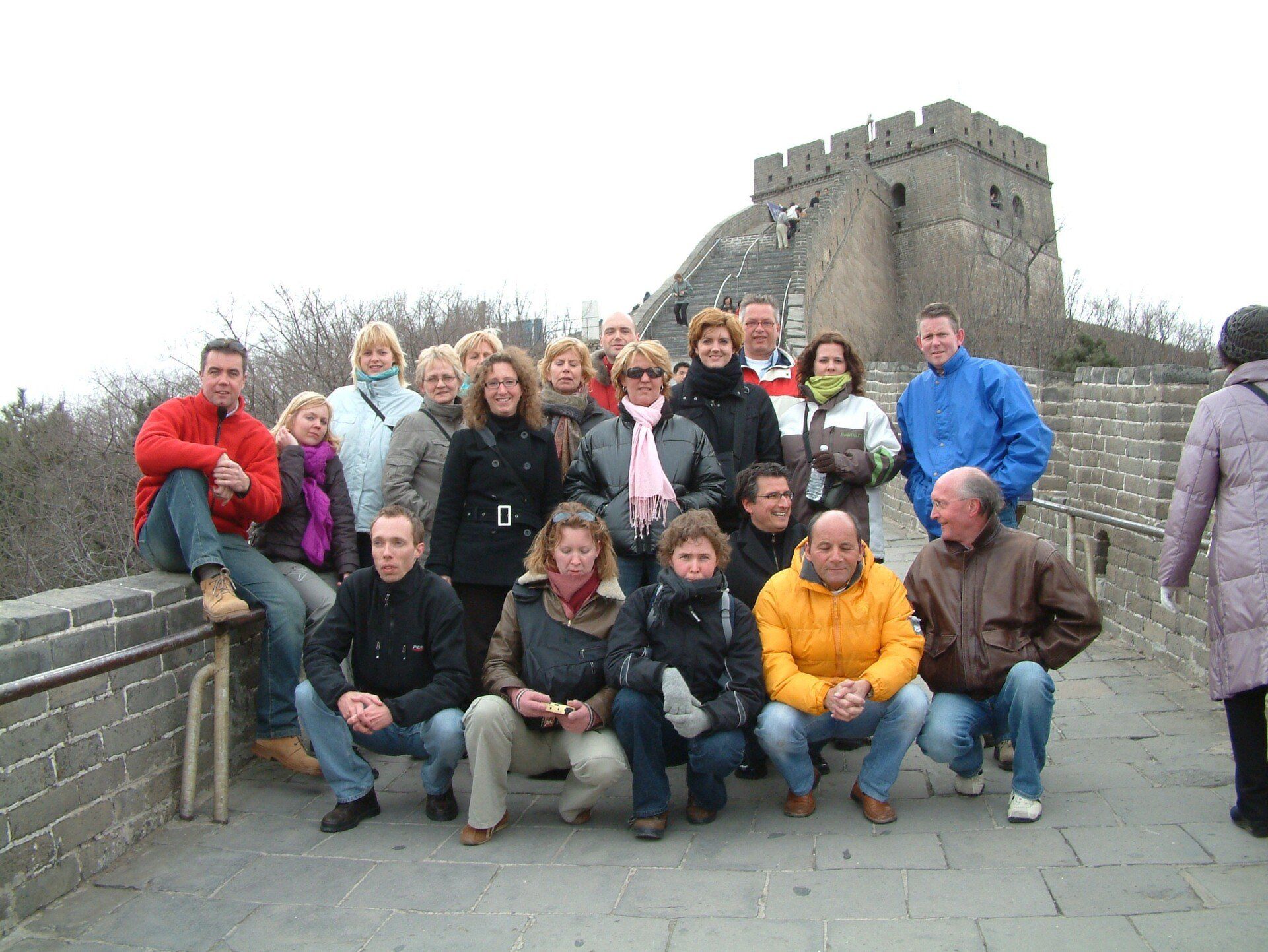 Een groep mensen poseert op de Chinese Muur; sommigen knielen of zitten, anderen staan.
