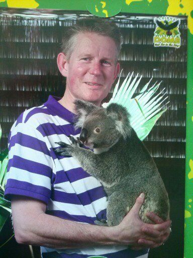 Man in gestreept shirt met een koala; groene achtergrond.