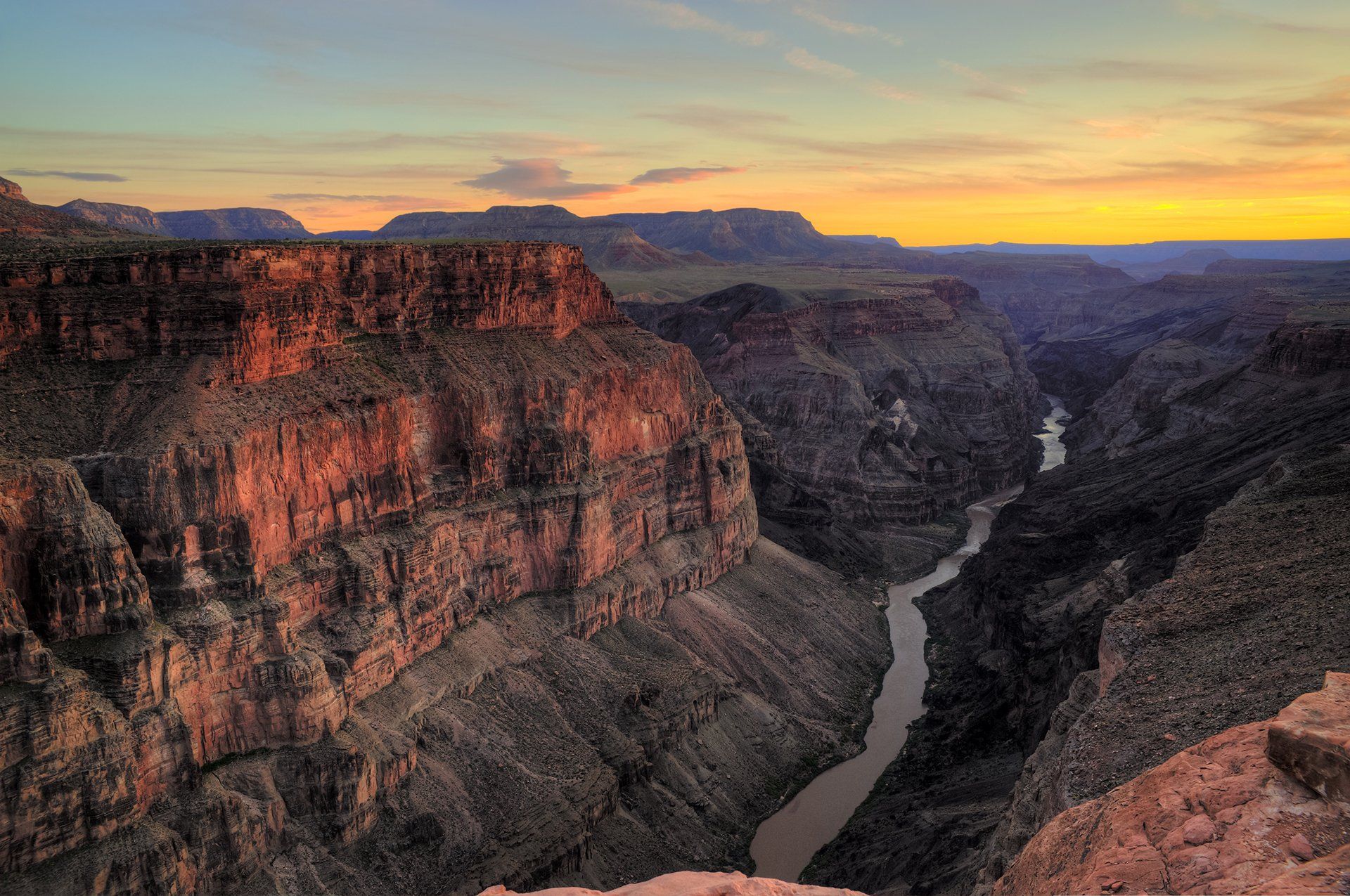 Zonsondergang boven een kloof. Rode en grijze rotsformaties omlijsten een rivier die door de kloof kronkelt.