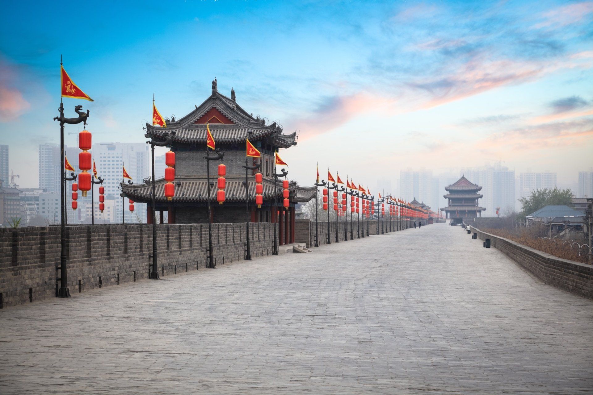 Stenen pad op de oude stadsmuur van Xi'an, China, met traditionele torens, rode lantaarns en vlaggen; bewolkte lucht.