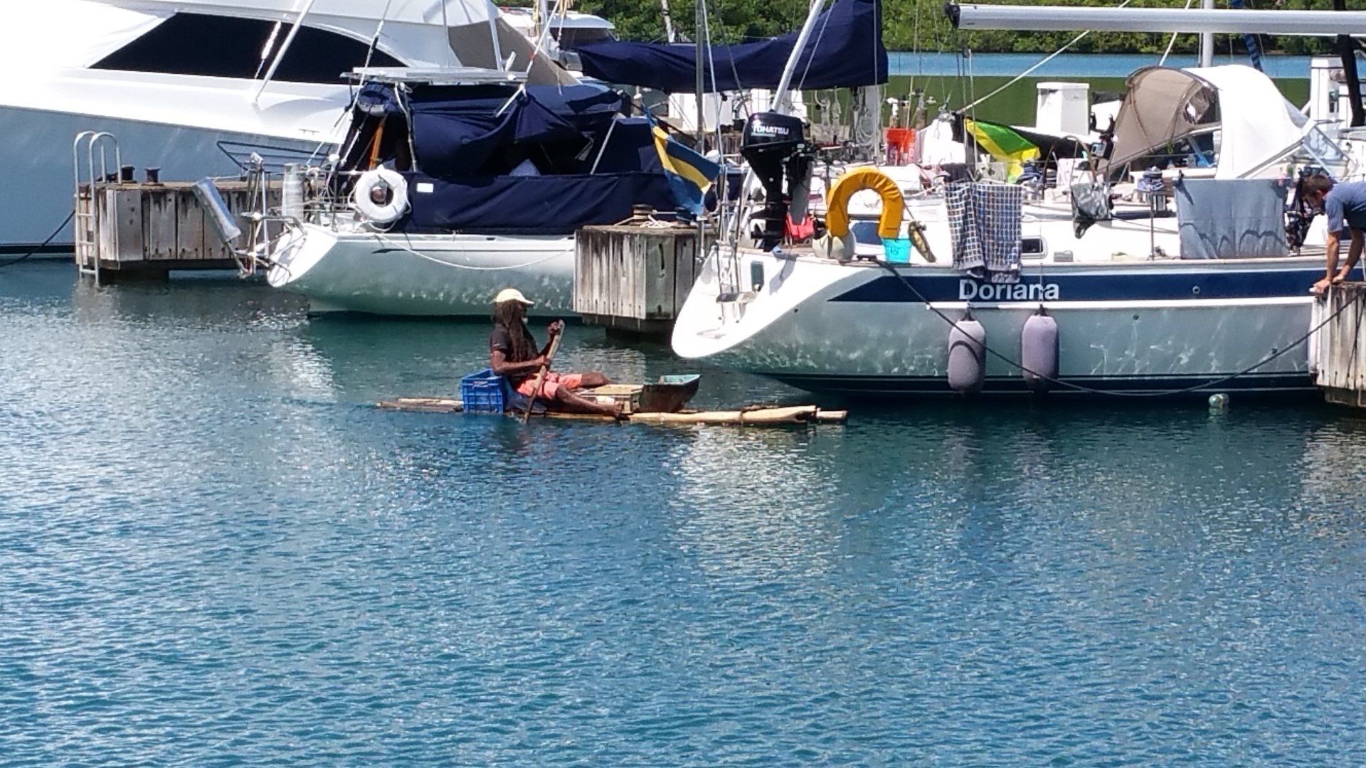 Boten aangemeerd in de haven, een persoon op een vlot in het water, met andere mensen in de buurt.