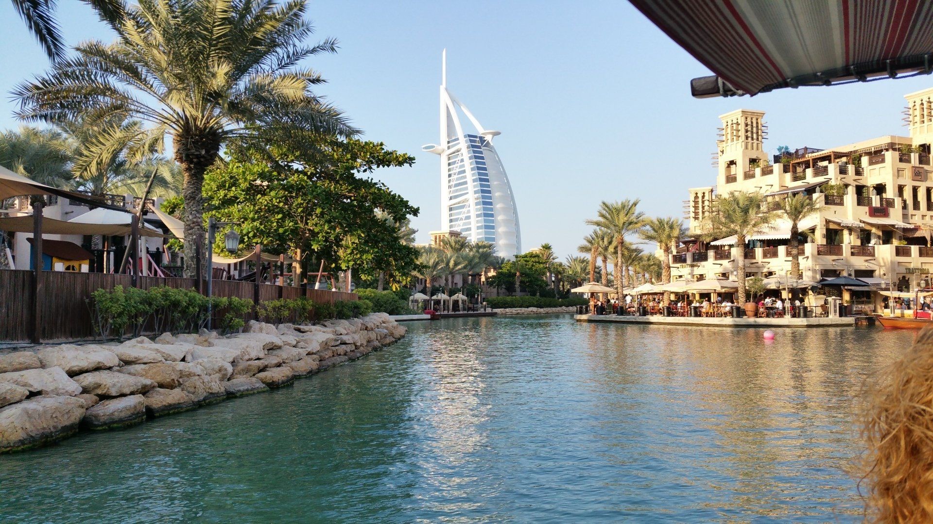 Een lagune in Dubai met het Burj Al Arab hotel op de achtergrond. Gebouwen en palmbomen omzomen het water.