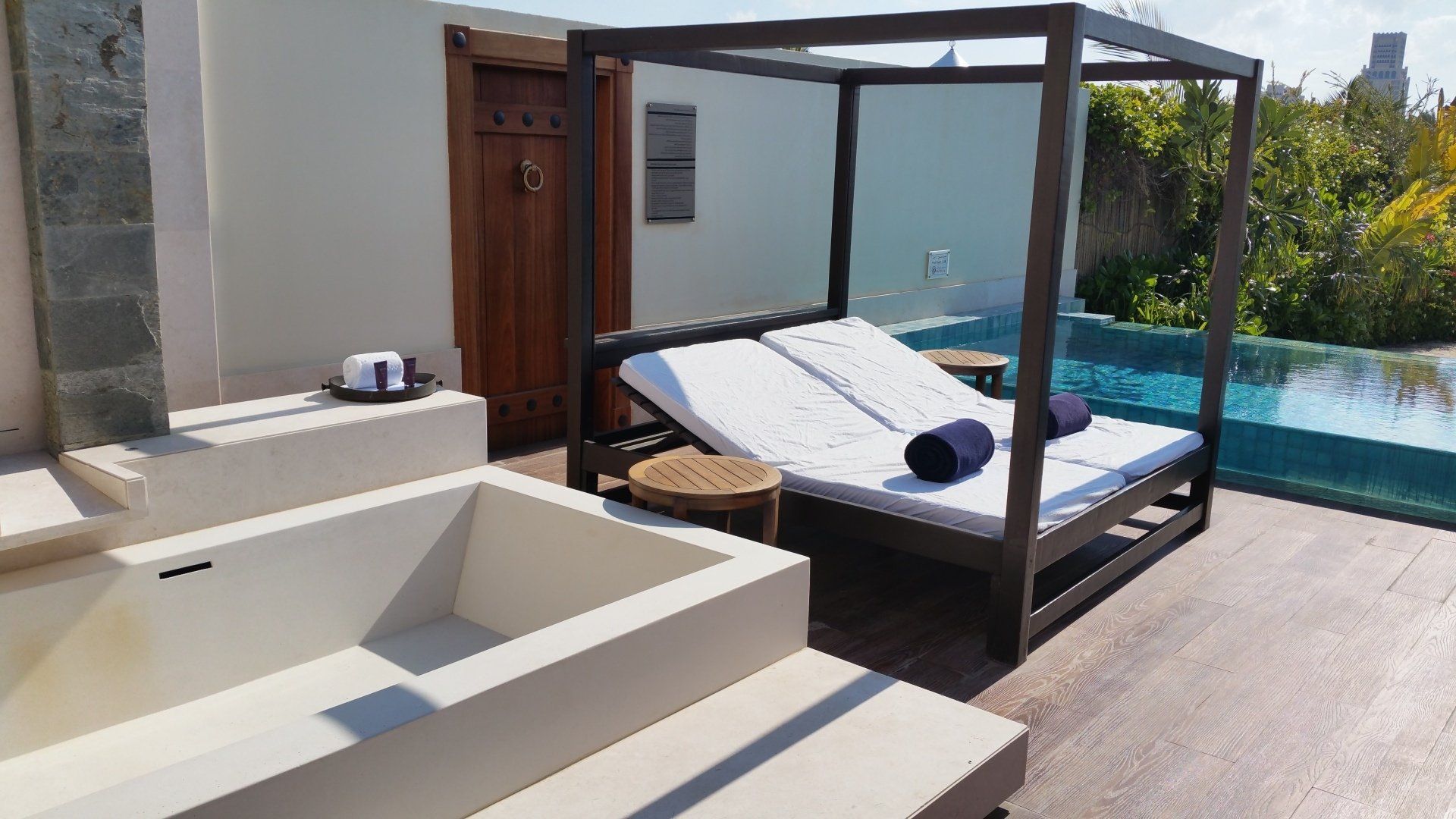 Buitenlounge met ligbed, jacuzzi en zwembad.