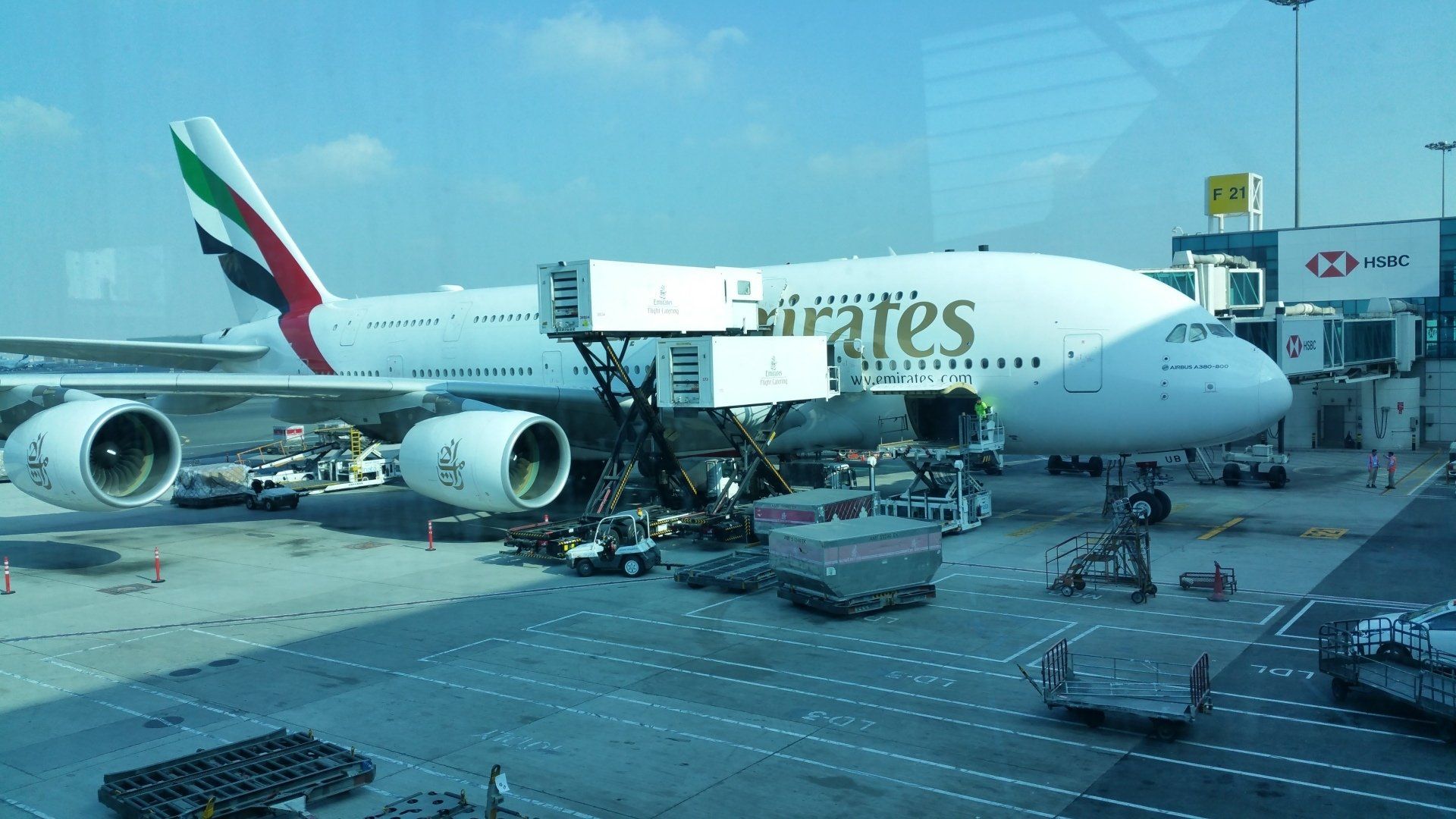 Een Emirates Airbus A380 staat aan de gate en wordt onderhouden door grondpersoneel, met een blauwe lucht op de achtergrond.