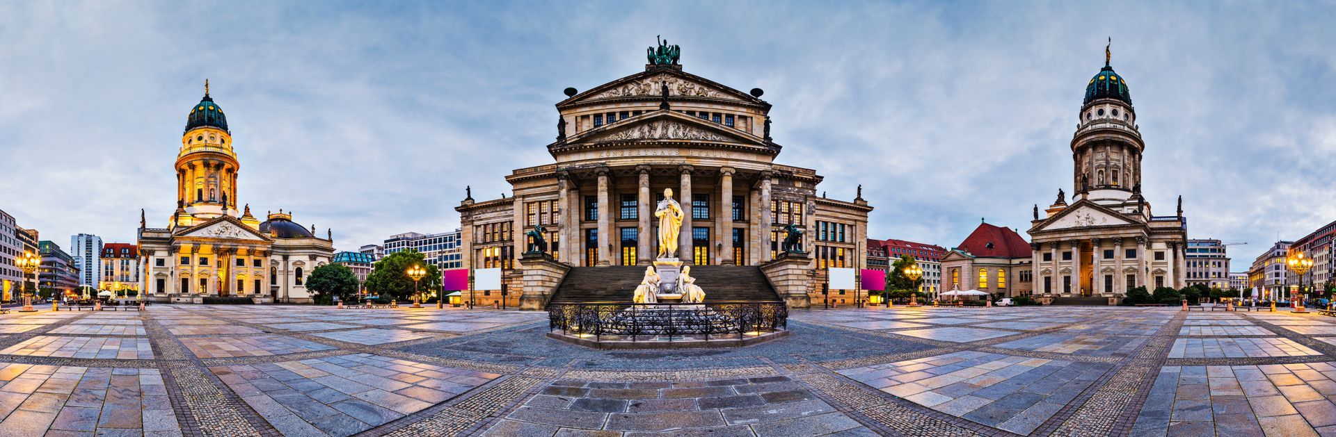 Een overzichtsfoto van het Gendarmenmarktplein in Berlijn, Duitsland, bij schemering, met drie grote gebouwen.