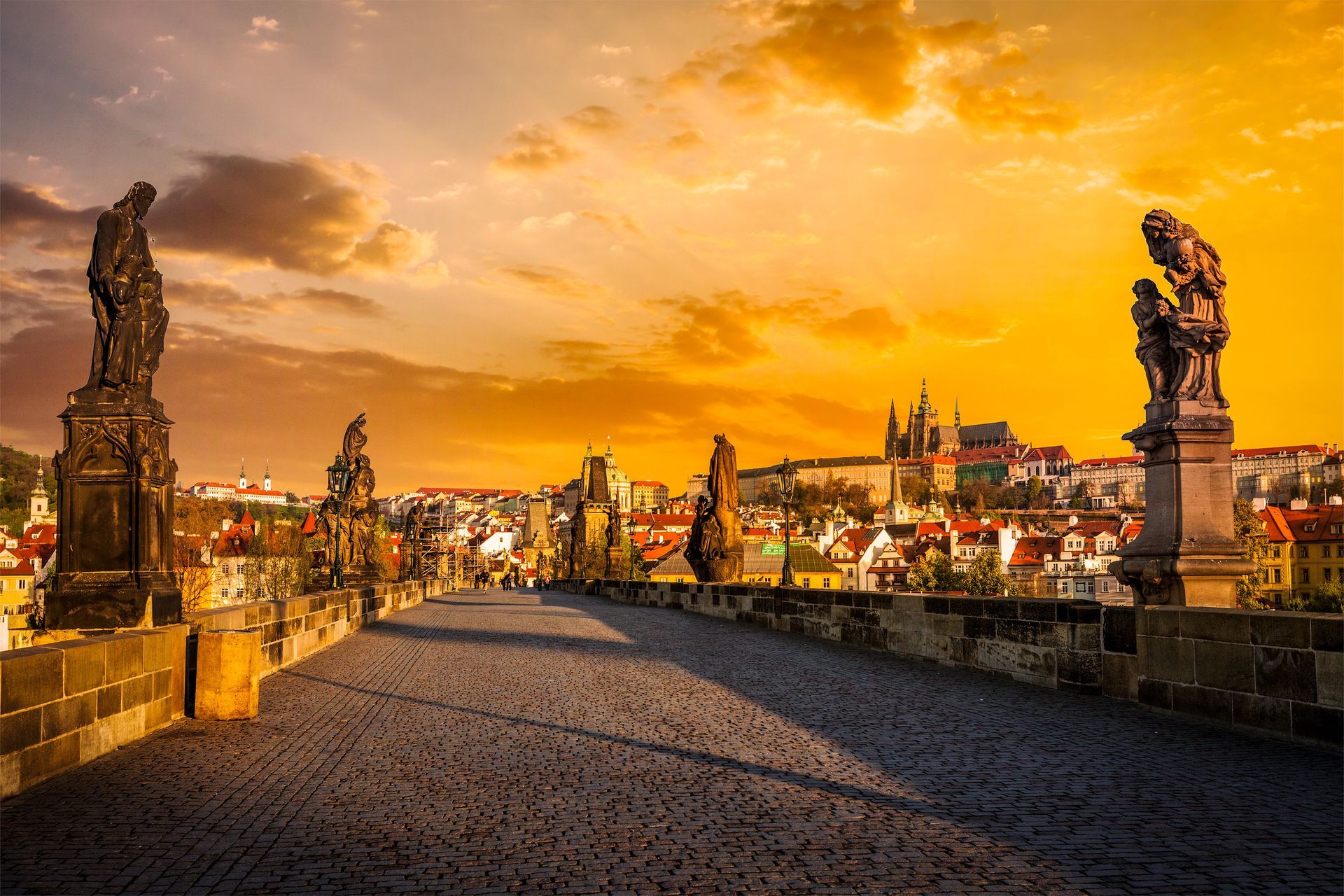 De Karelsbrug in Praag bij zonsondergang, met beelden langs de brug, de skyline van de stad tegen een oranje lucht.